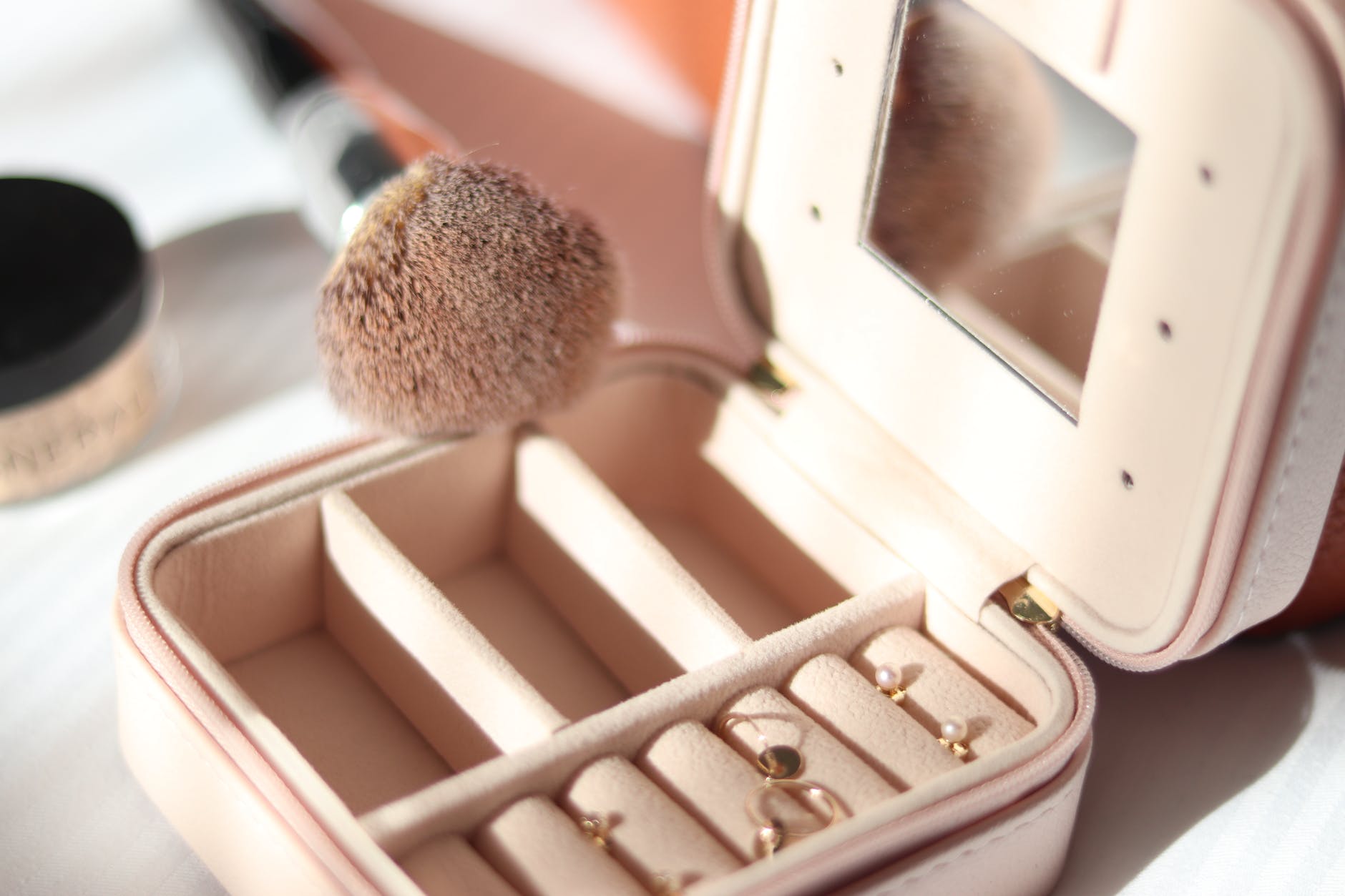 A jewelry box with jewelries inside and a makeup brush beside it