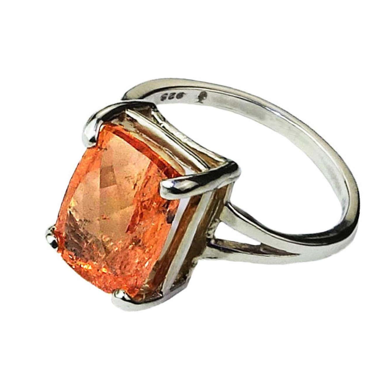 A large orange imperial topaz is held by a silver ring on a white background