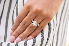 A pear shaped diamond wedding ring on a lady's left hand with light pink nails and resting on striped dress 