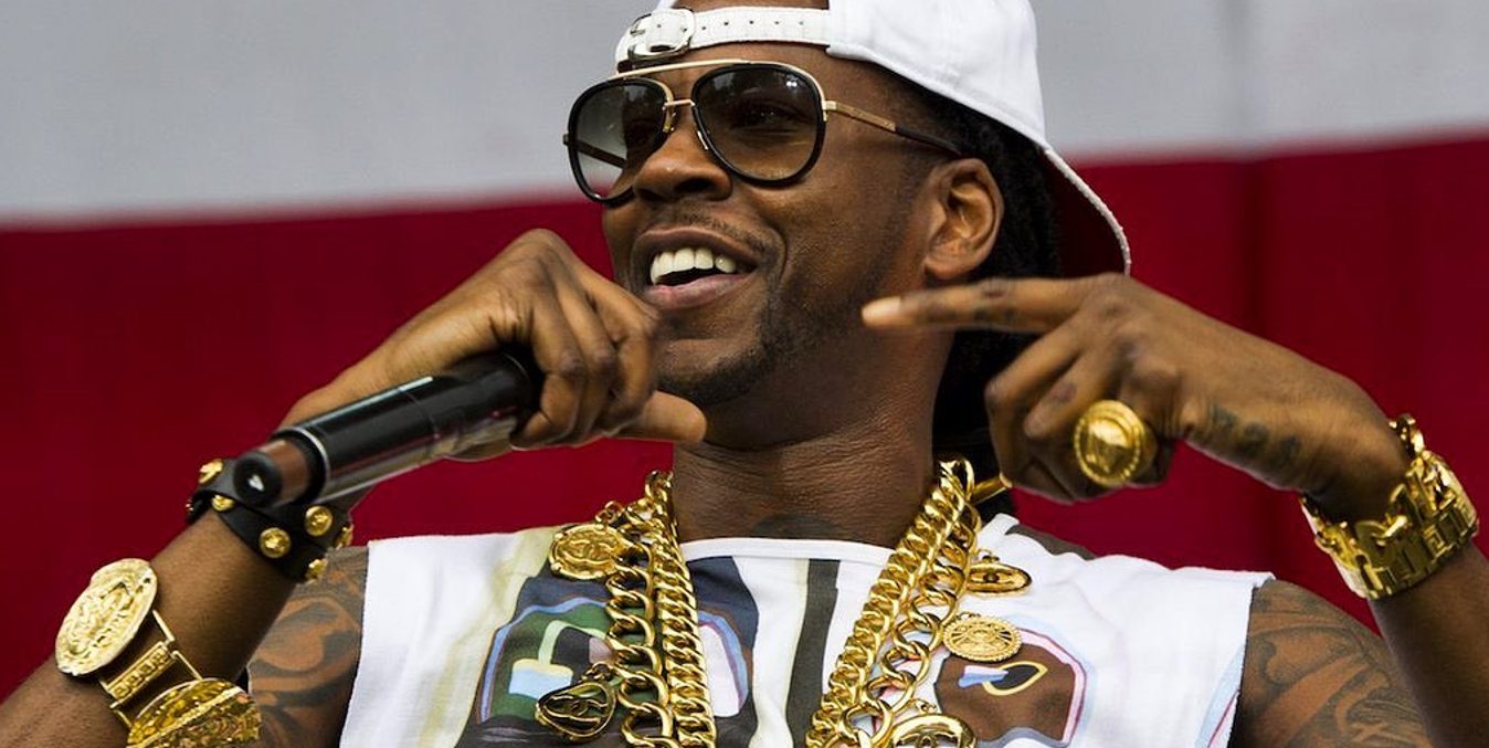 Rapper 2 Chainz wearing thick gold chains, gold bracelets on both arms and one oversized gold ring