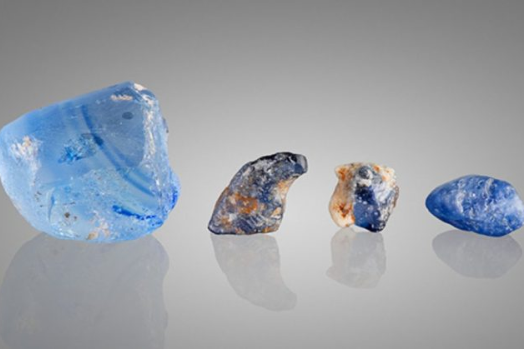 This set includes a 48.63 ct piece of manmade glass (left), 9.17 and 6.21 ct laboratory-grown sapphires with resin matrix imitation on the surface (center), and an 8.46 ct natural blue sapphire rough (right) (right)