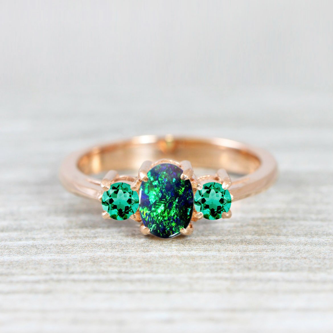 Gold ring with black opal as the stone and two emeralds on the side