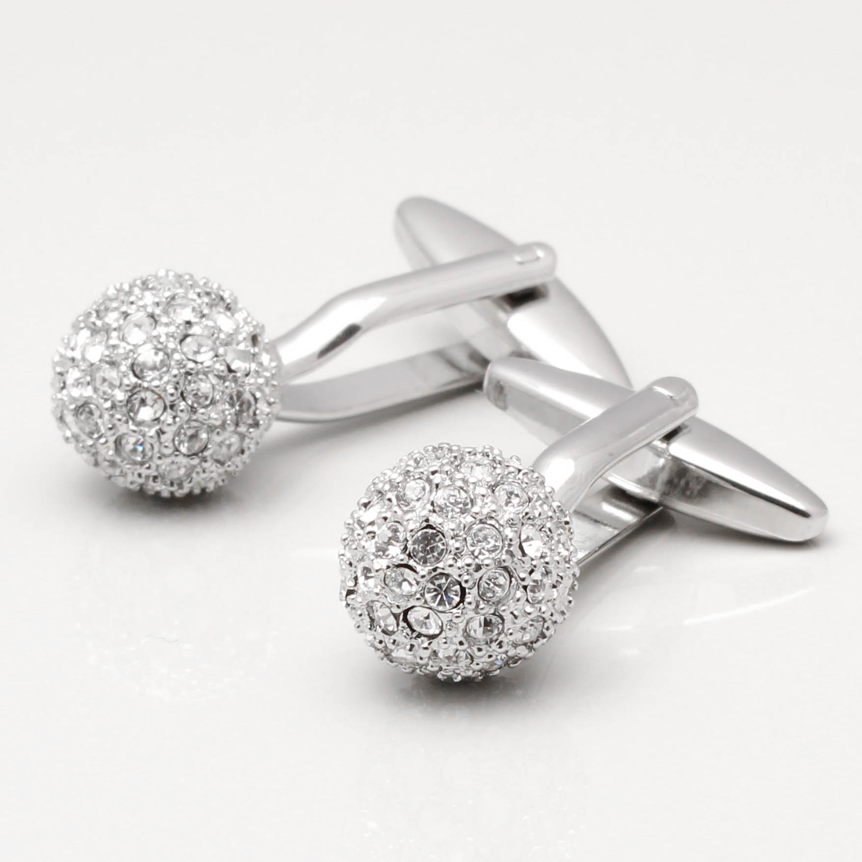 A pair of cufflinks made of clear crystal are displayed on a white table