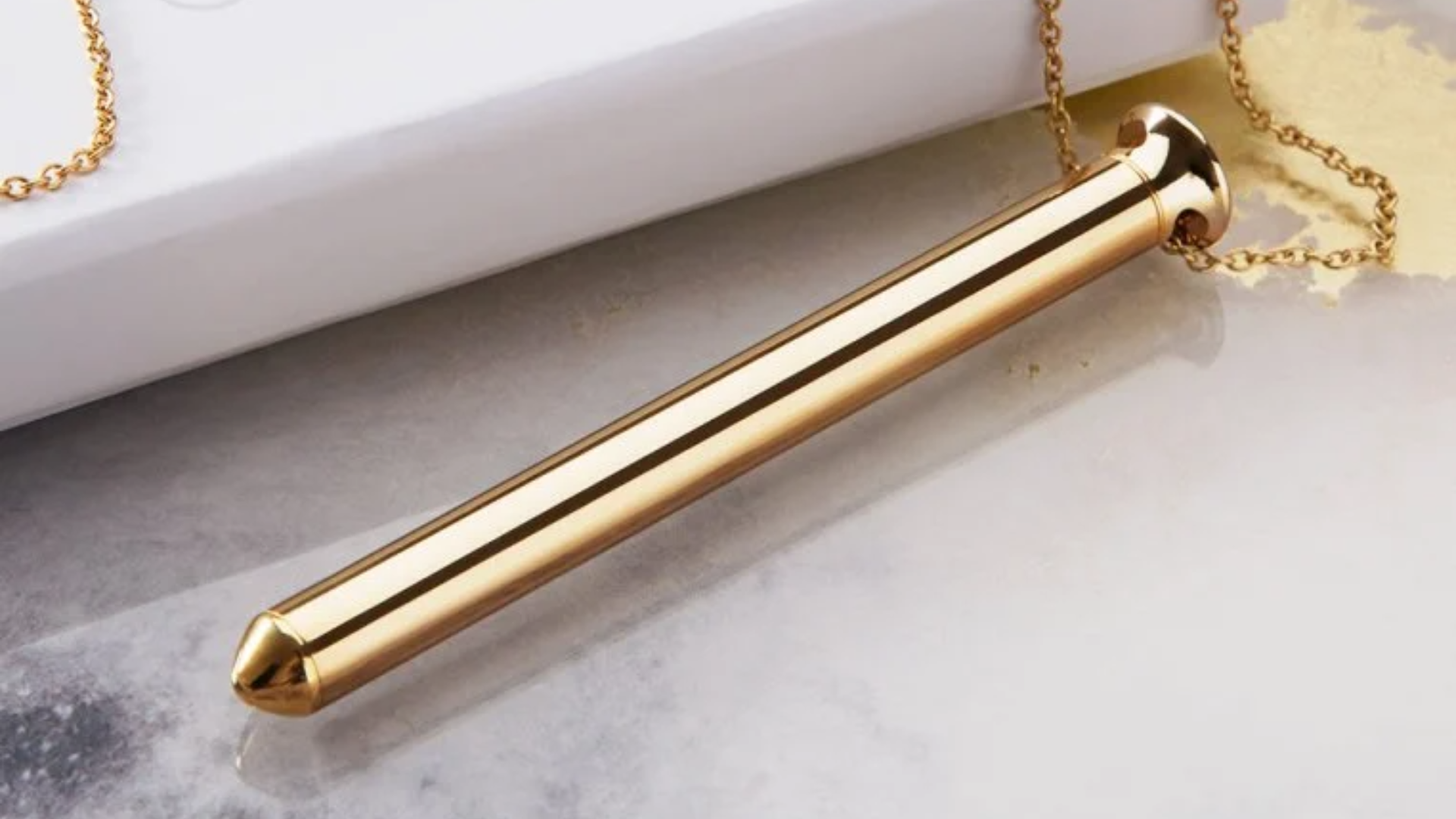 A gold Vibrator Necklace placed on top of the table with a box beside it