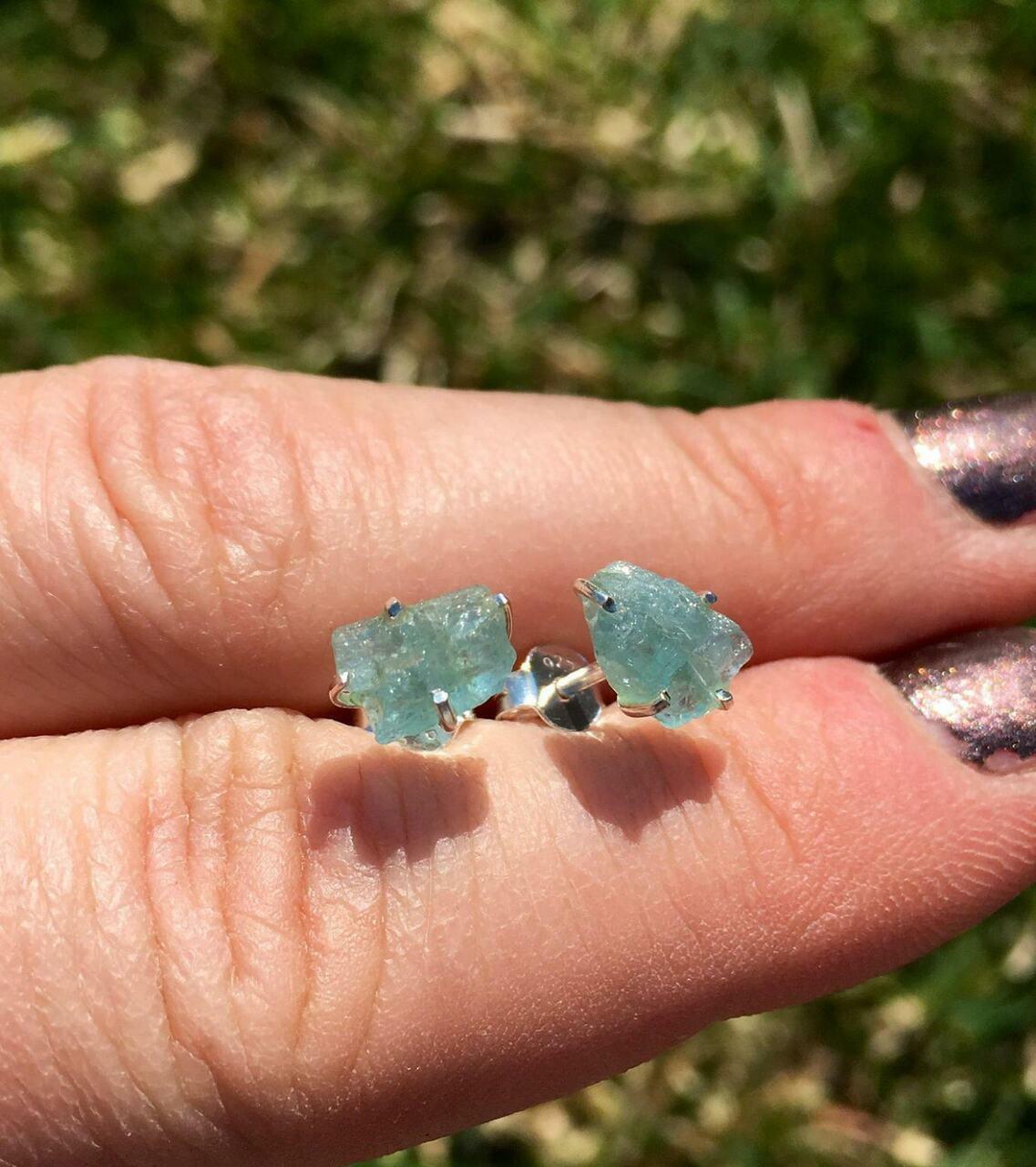 A lady holding raw aquamarine studs between her two fingers