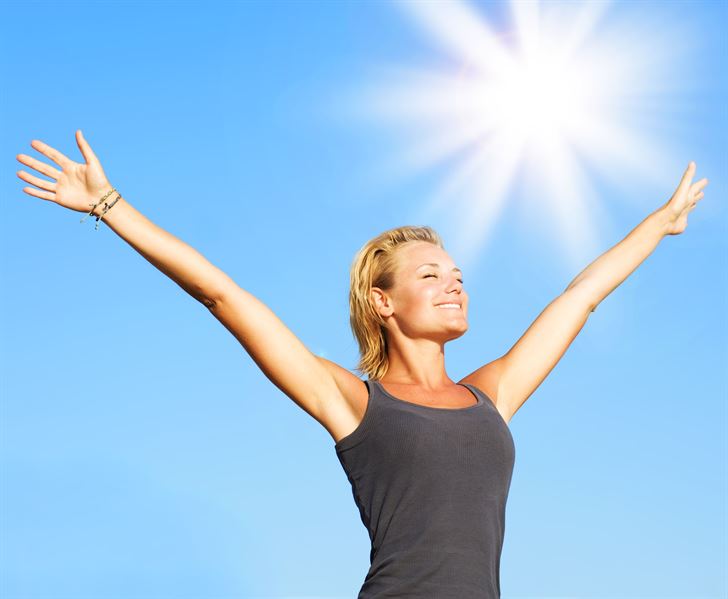 Under the blue sky and sun, the girl raises her hands while on her sleeveless black top