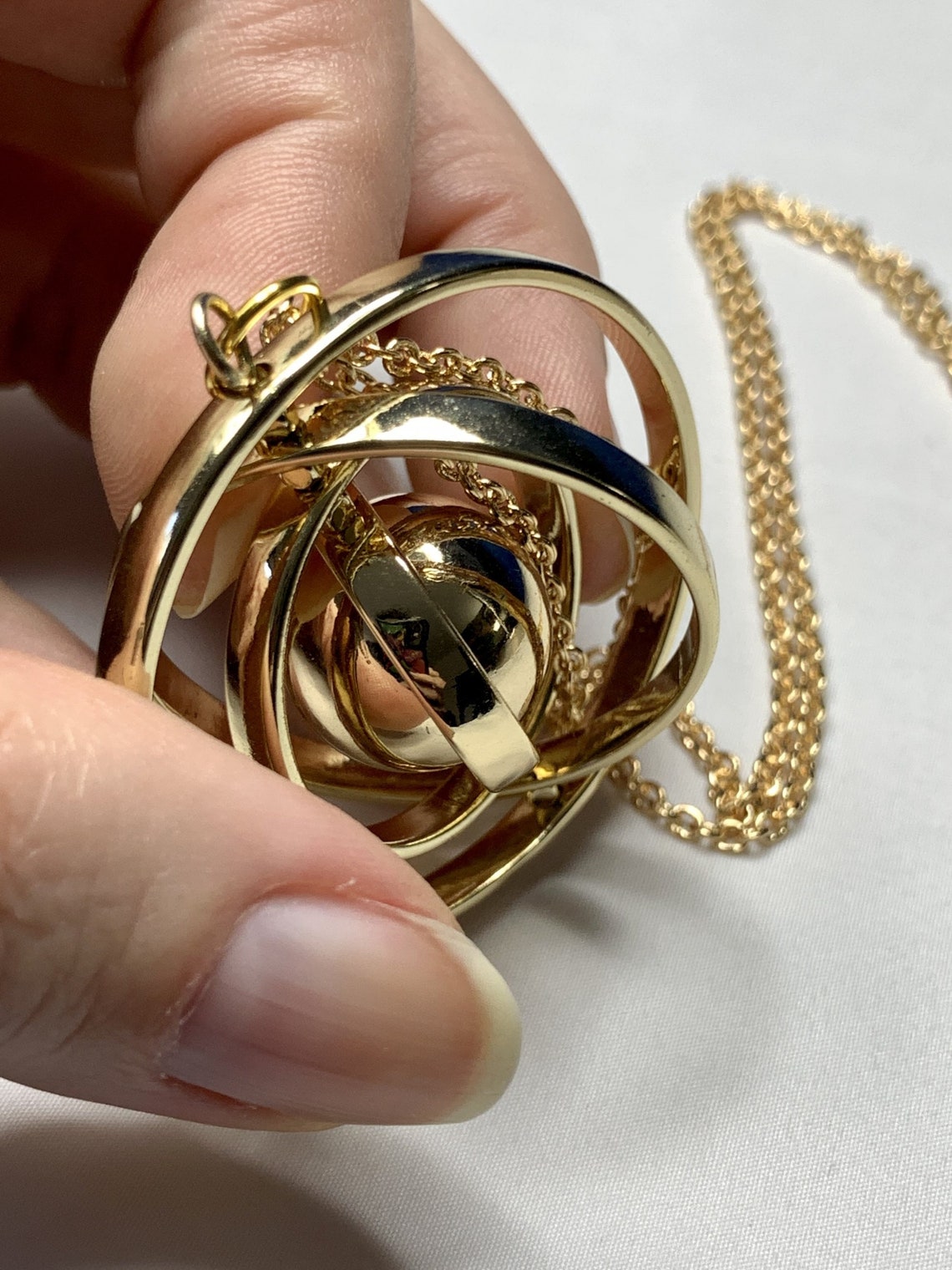 A zoom-in image of a hand holding a revolving planet pendant with gold chain