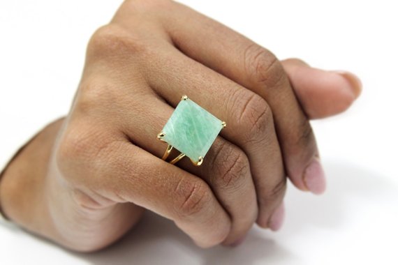 A black woman's ring finger is adorned with a square amazonite ring