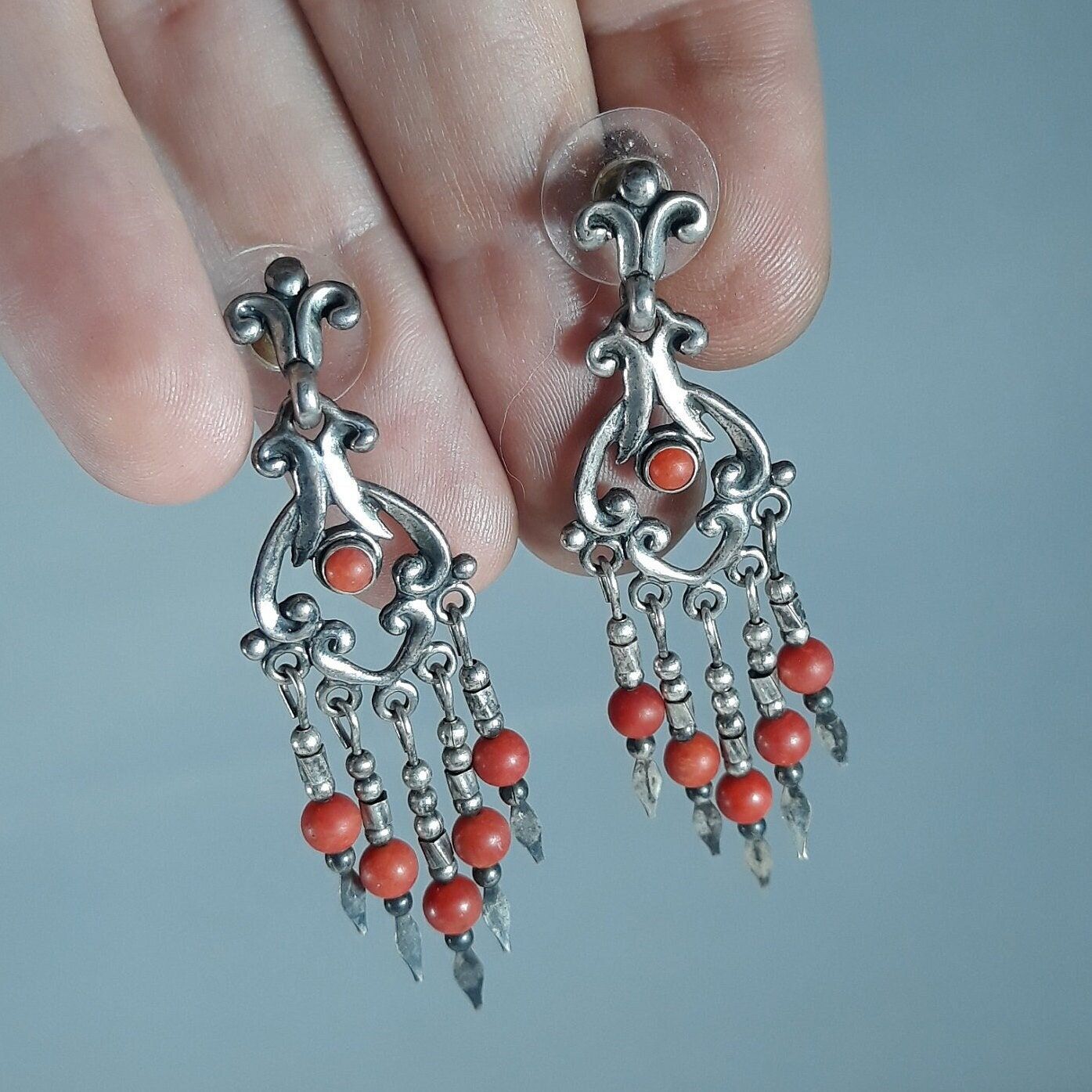 A woman holding a pair of silver earrings with orange beads