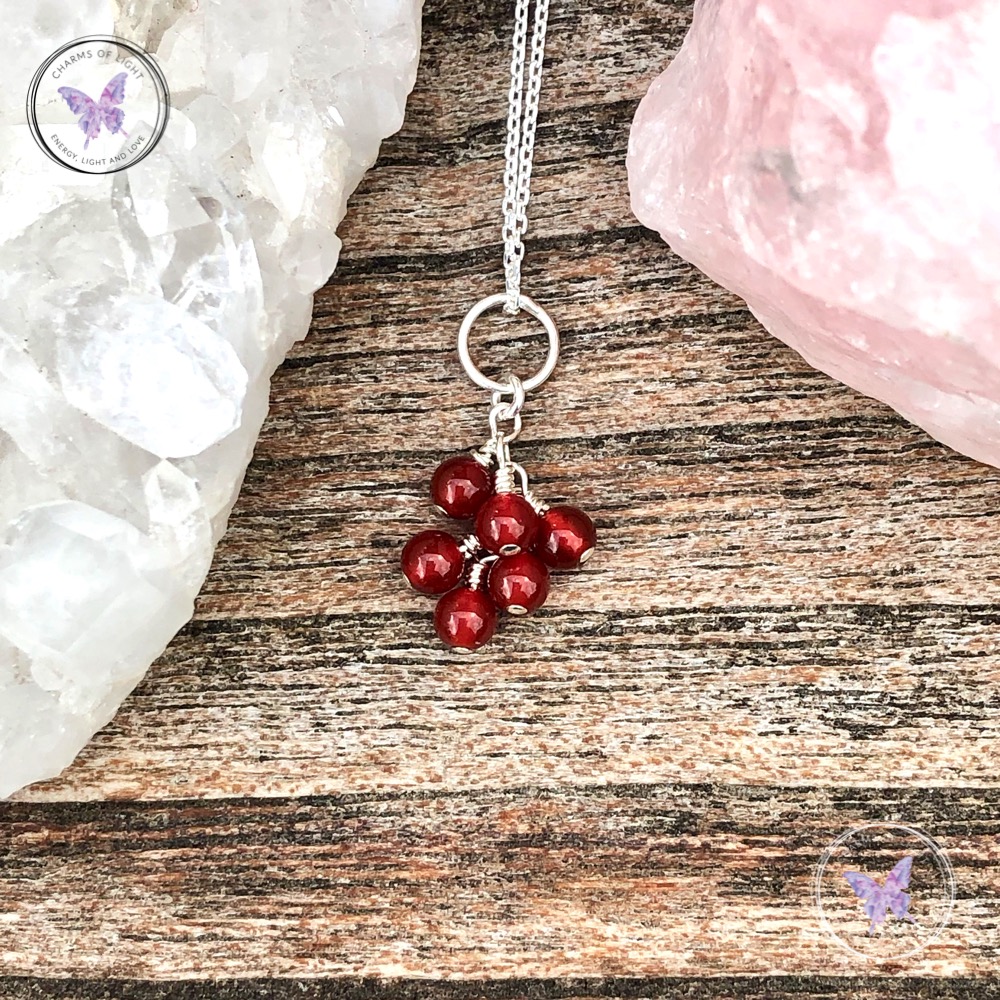 A pendant with ruby beads is set in a wood table with crystals beside it