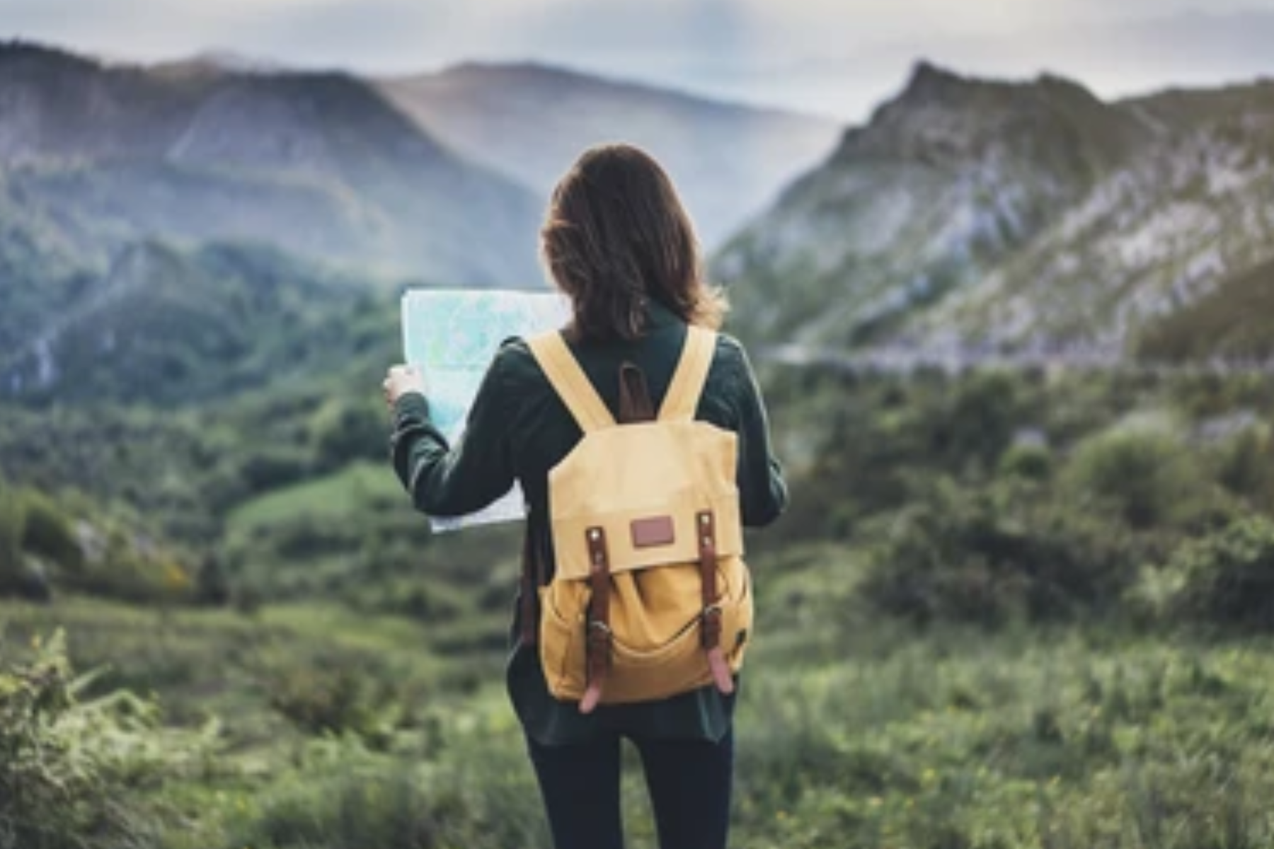 In front of huge mountains, a woman traveling with her backpack and a map