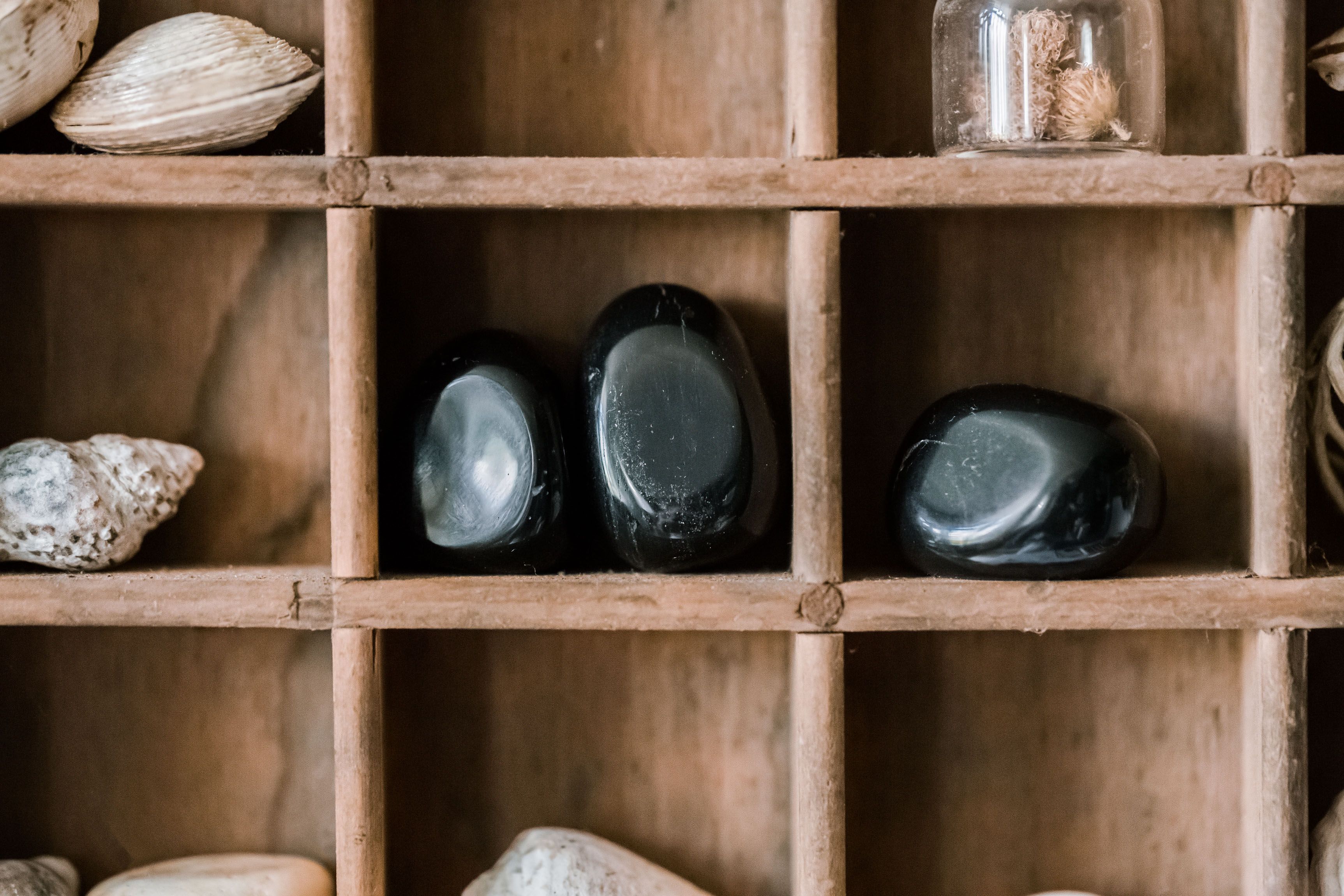 Three Black Onyx feng shui on a wooden shelf together with other gemstones and a shell beside