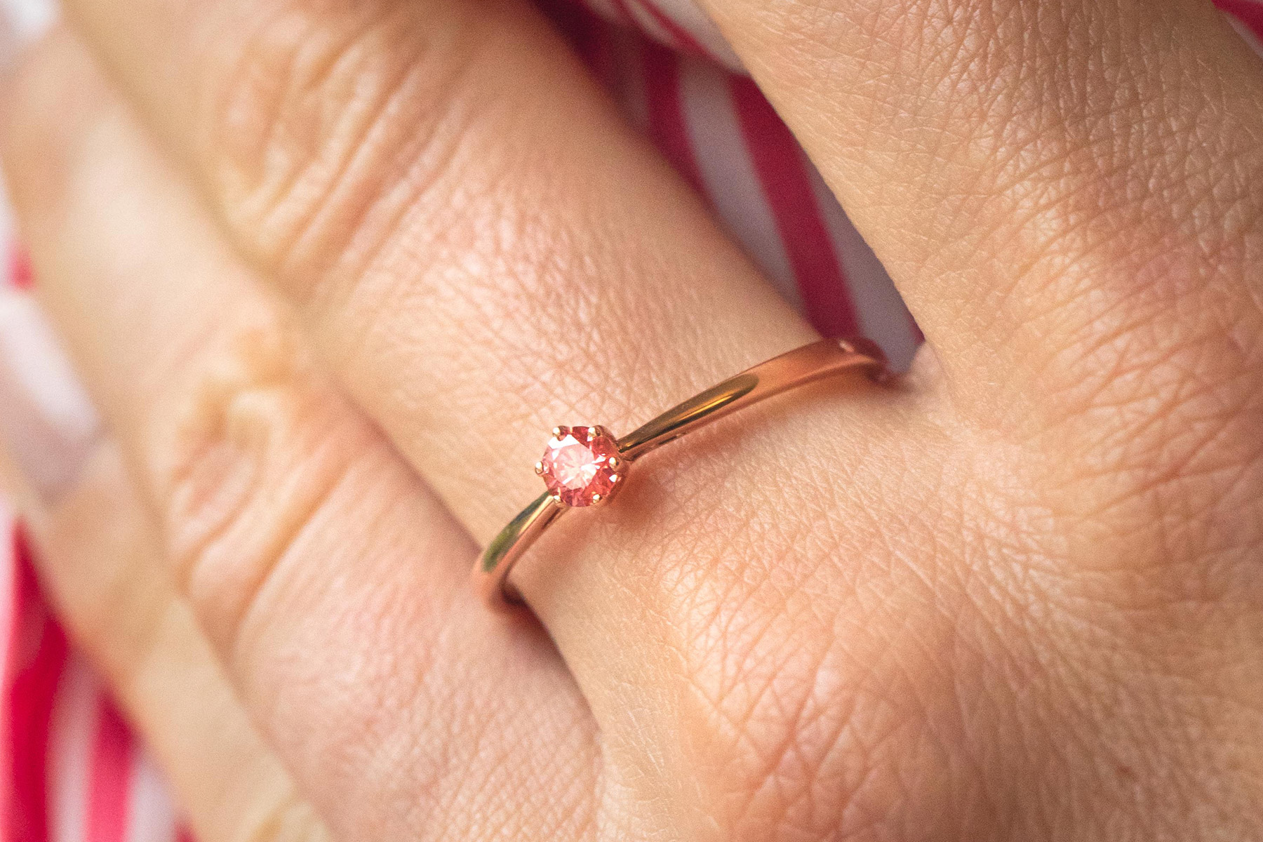 On the woman's ring finger is a gold ring with a lab-grown pink diamond