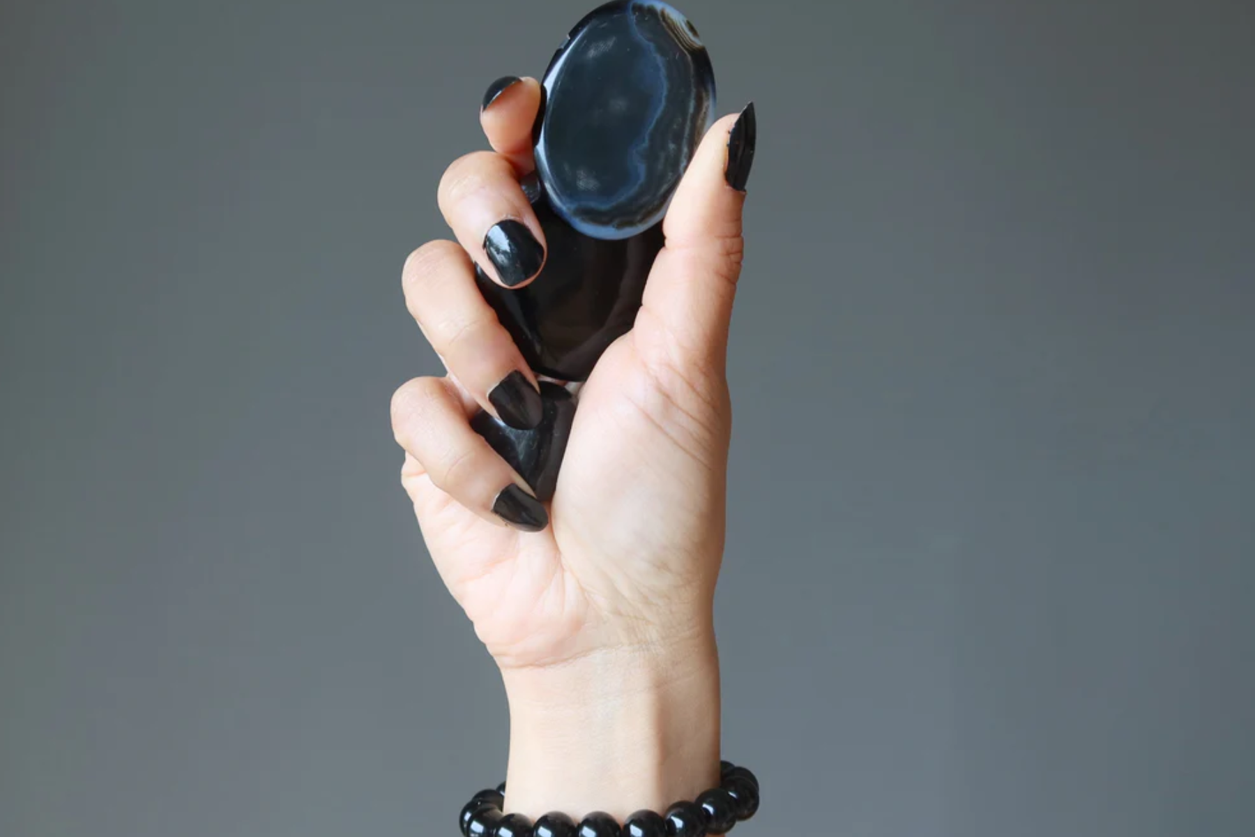 A woman's hand lifting three onyx stones on a gray setting