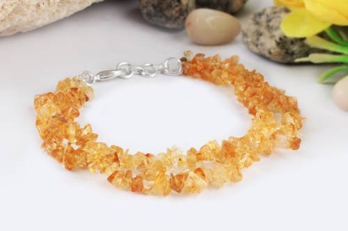 A topaz bracelet is displayed on a table with stones and a flower