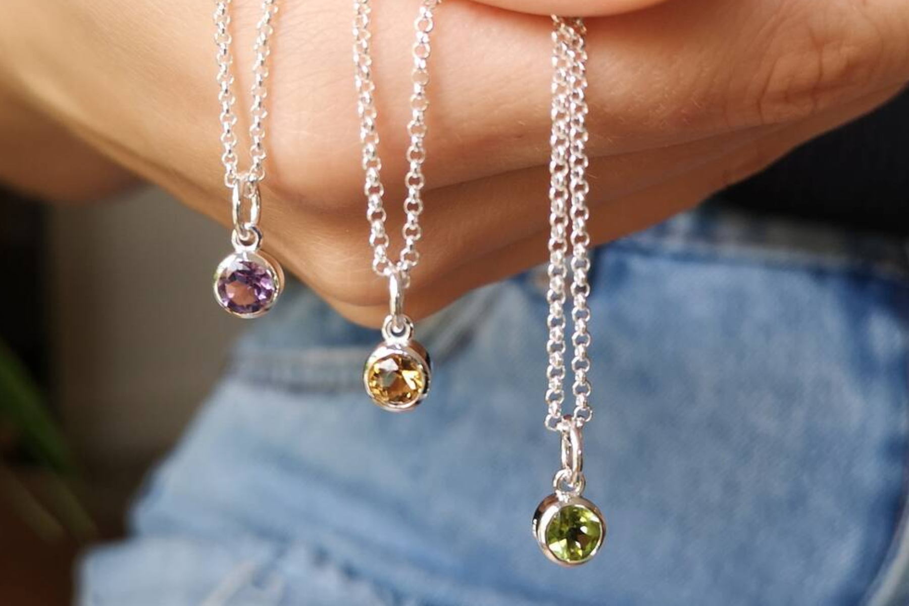 A person's hand holding three birthstone necklaces