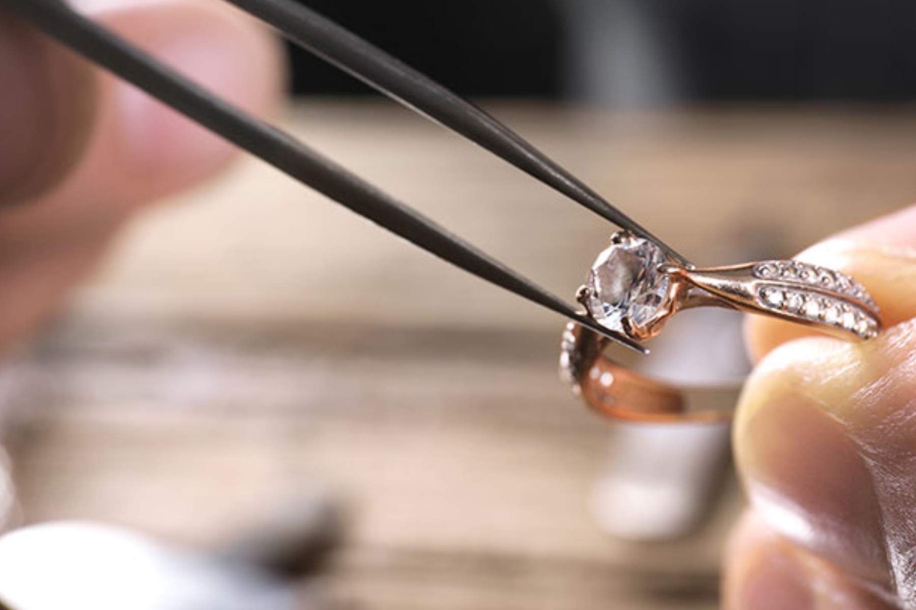 A person's hand placing a diamond stone on a ring with the help of a prong
