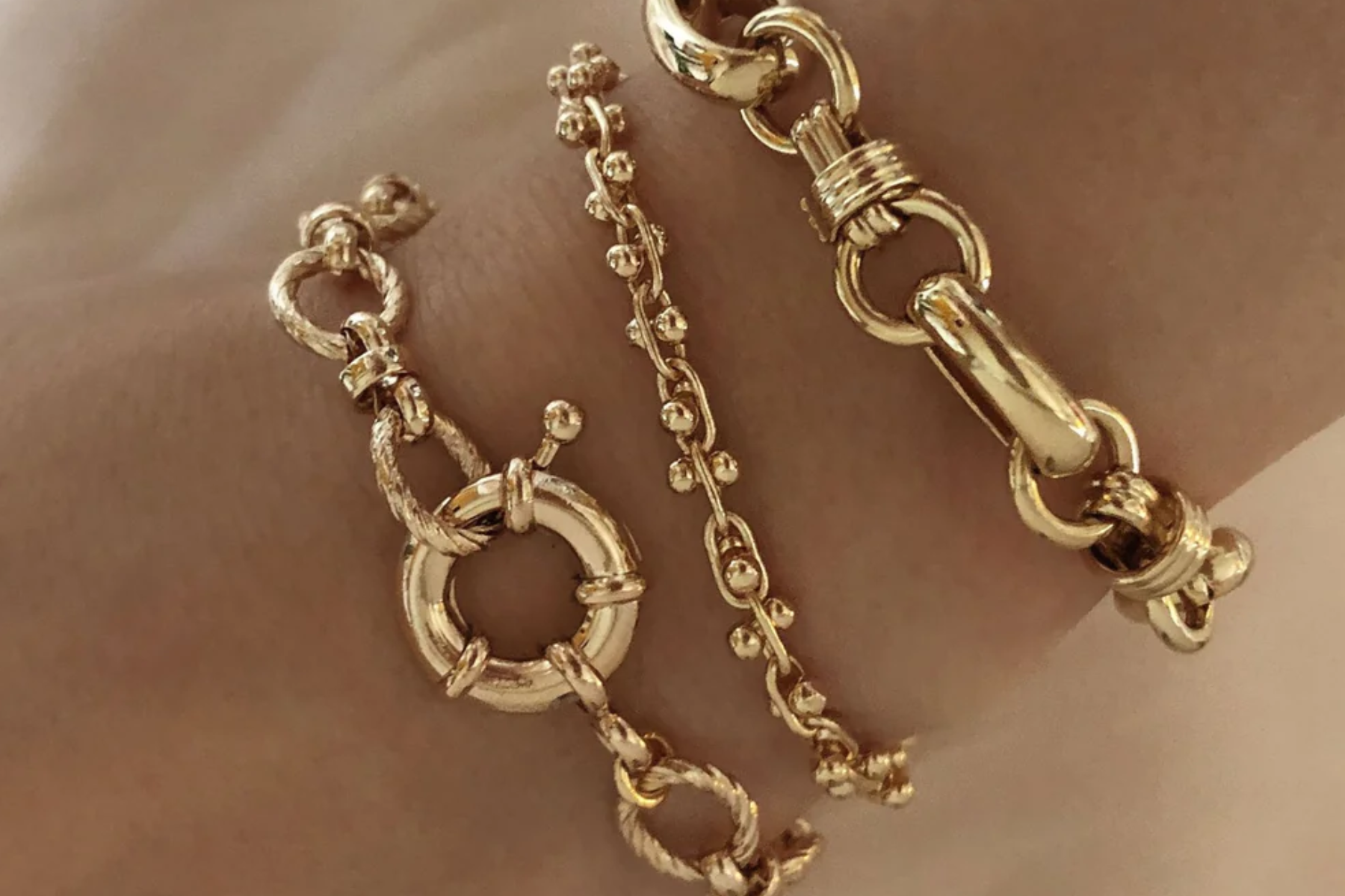 An individual's wrist is adorned with three gold chunky bracelets