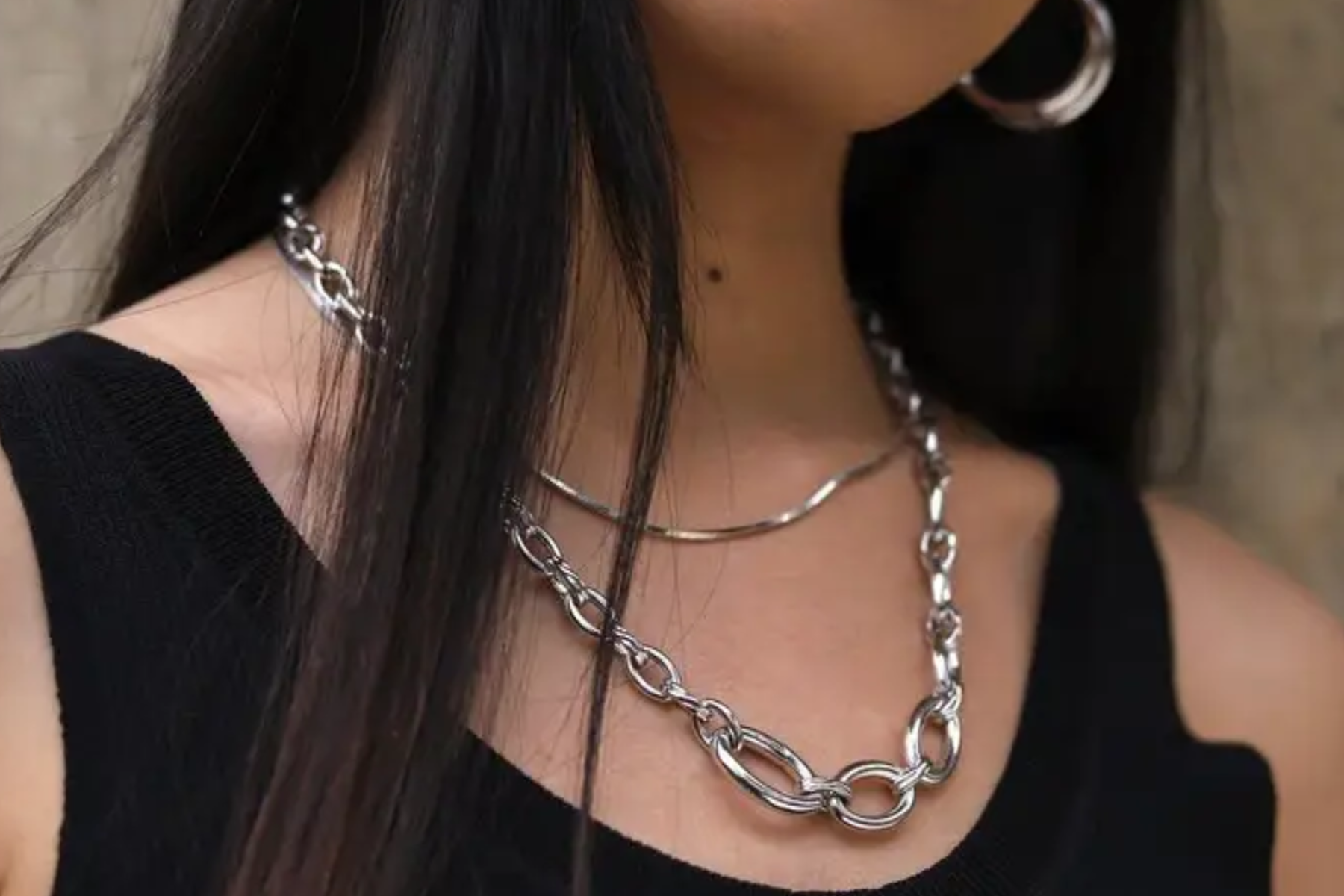 A woman with a black sleeveless shirt, silver necklaces, and silver earrings