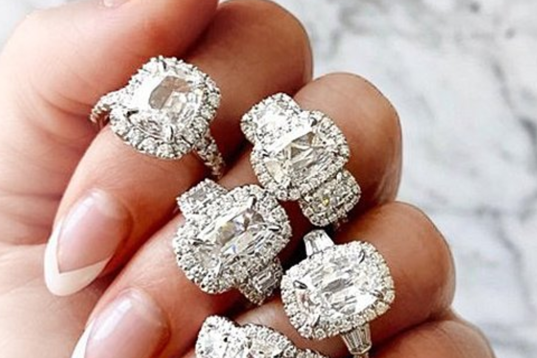 Five halo diamond rings adorn the fingers of a woman