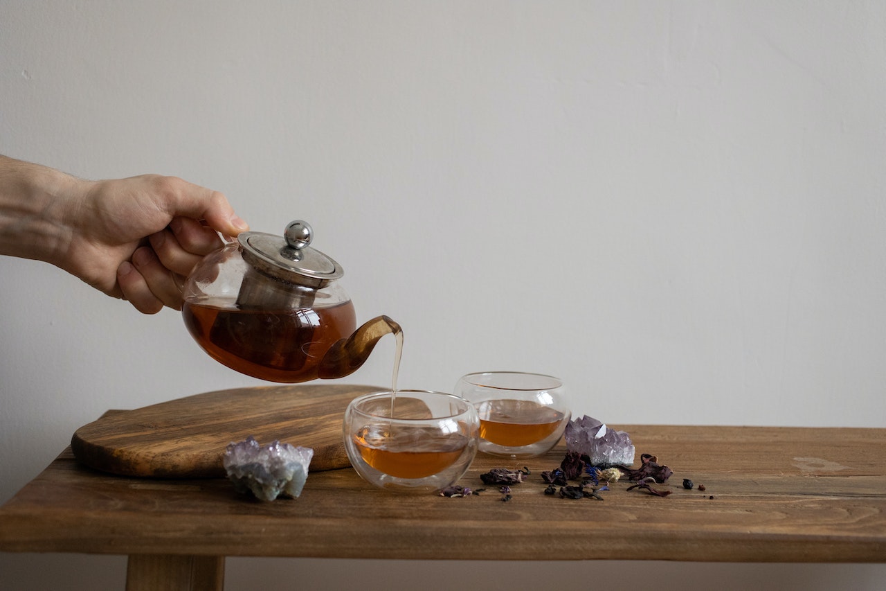Hand Pouring Tea to Glasses near Crystals