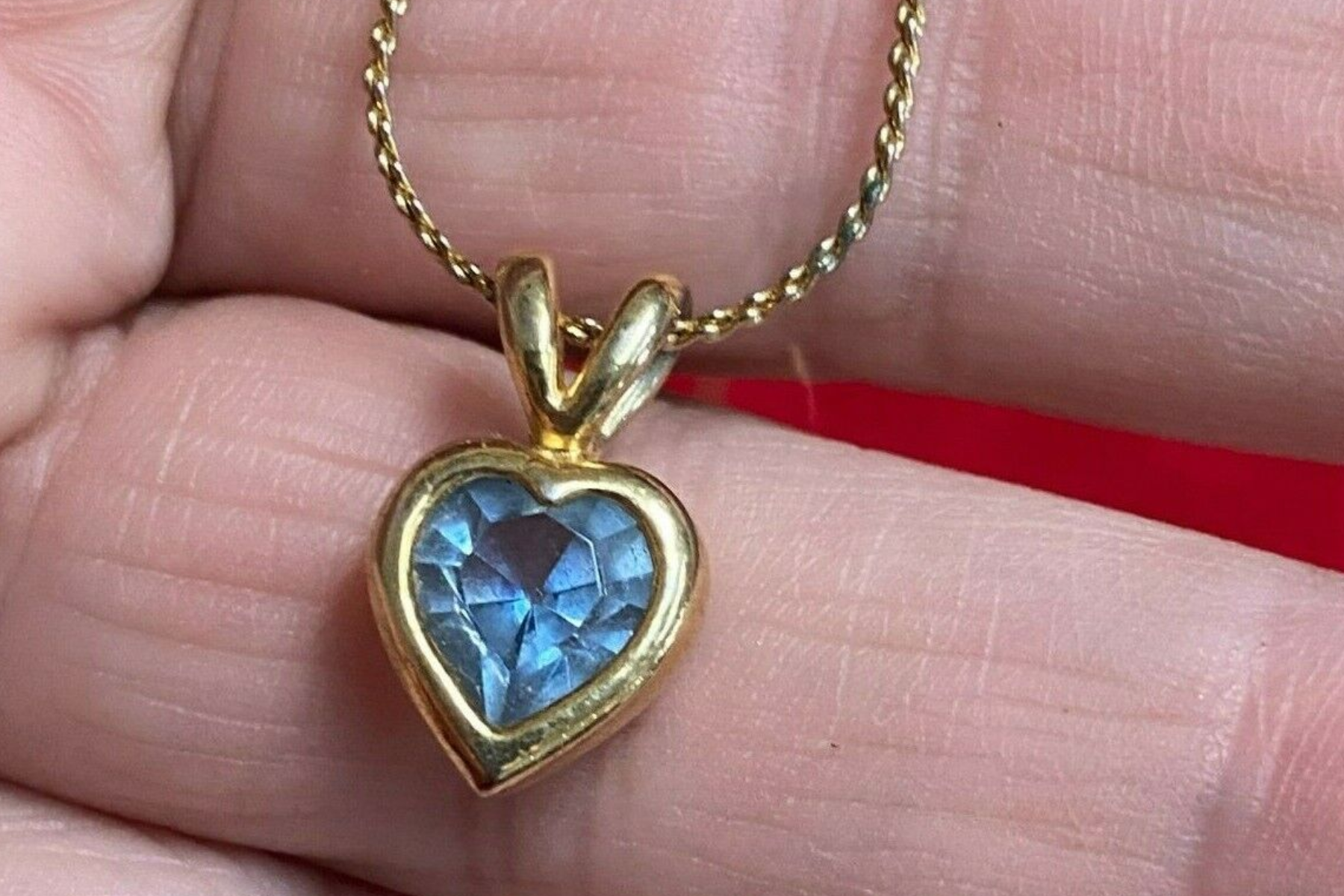 A woman's palm with a blue stone set in a gold heart pendant