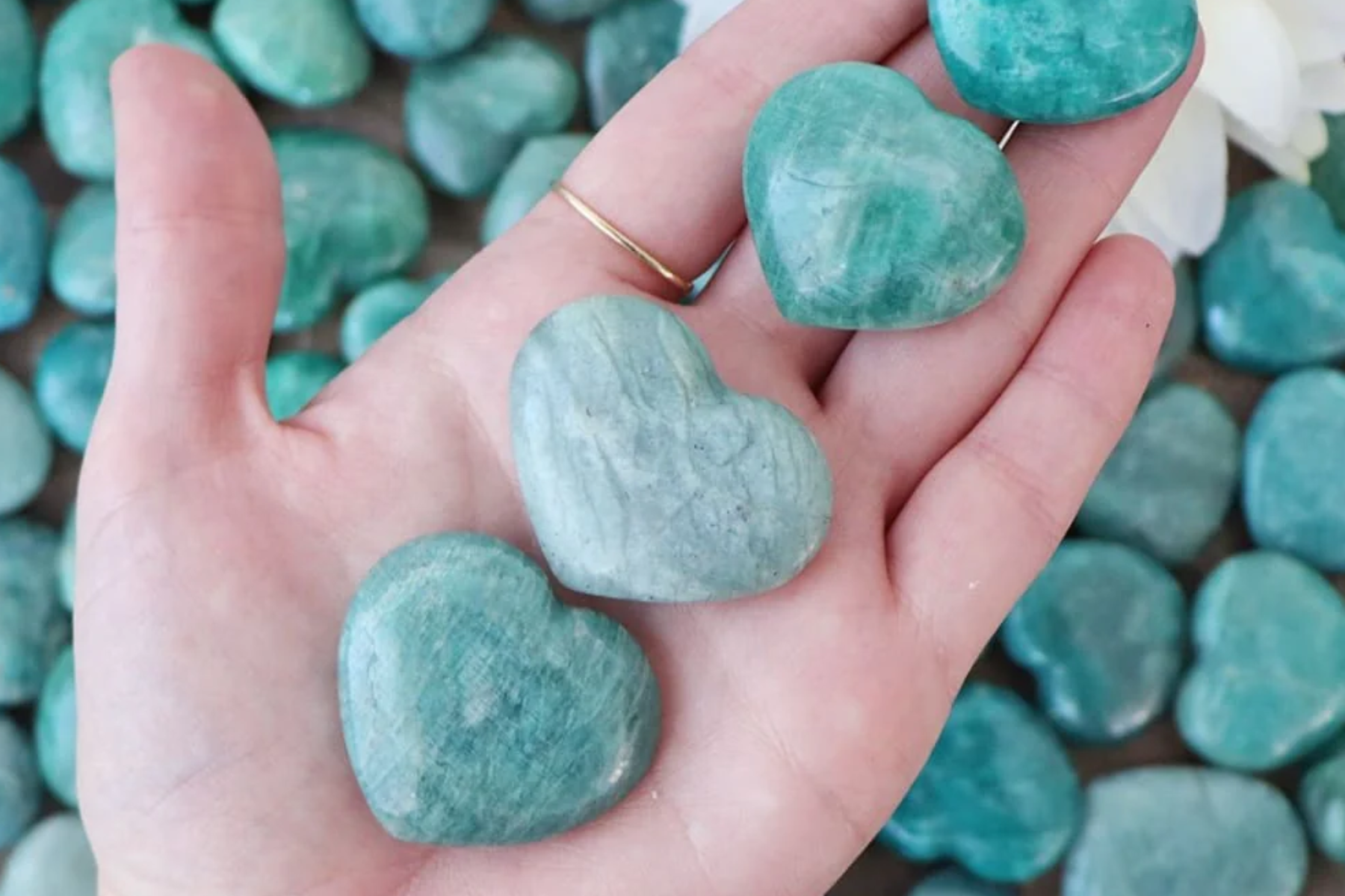A woman's hand holding four heart-shaped amazonite stones
