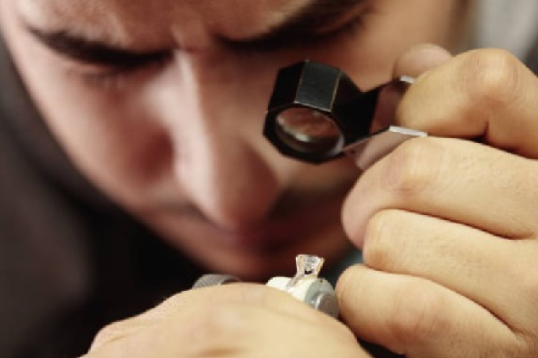 A man examines a platinum and diamond stone ring with a small magnifying glass