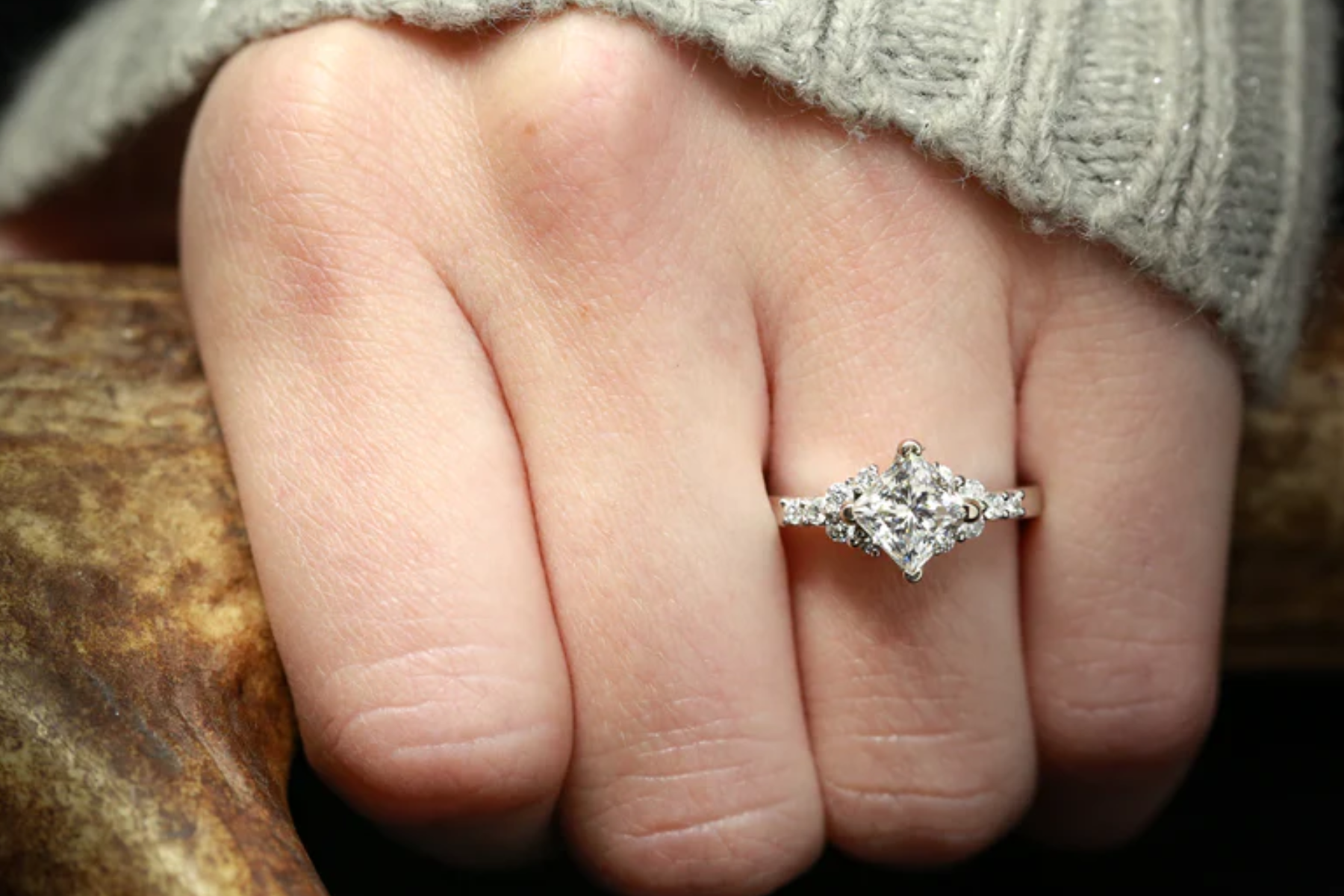 A woman's ring finger is adorned with a princess cut kite diamond ring