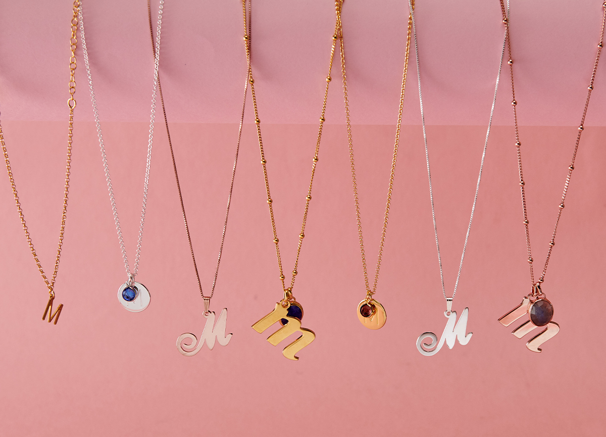 Seven different designs of "M" initial necklaces