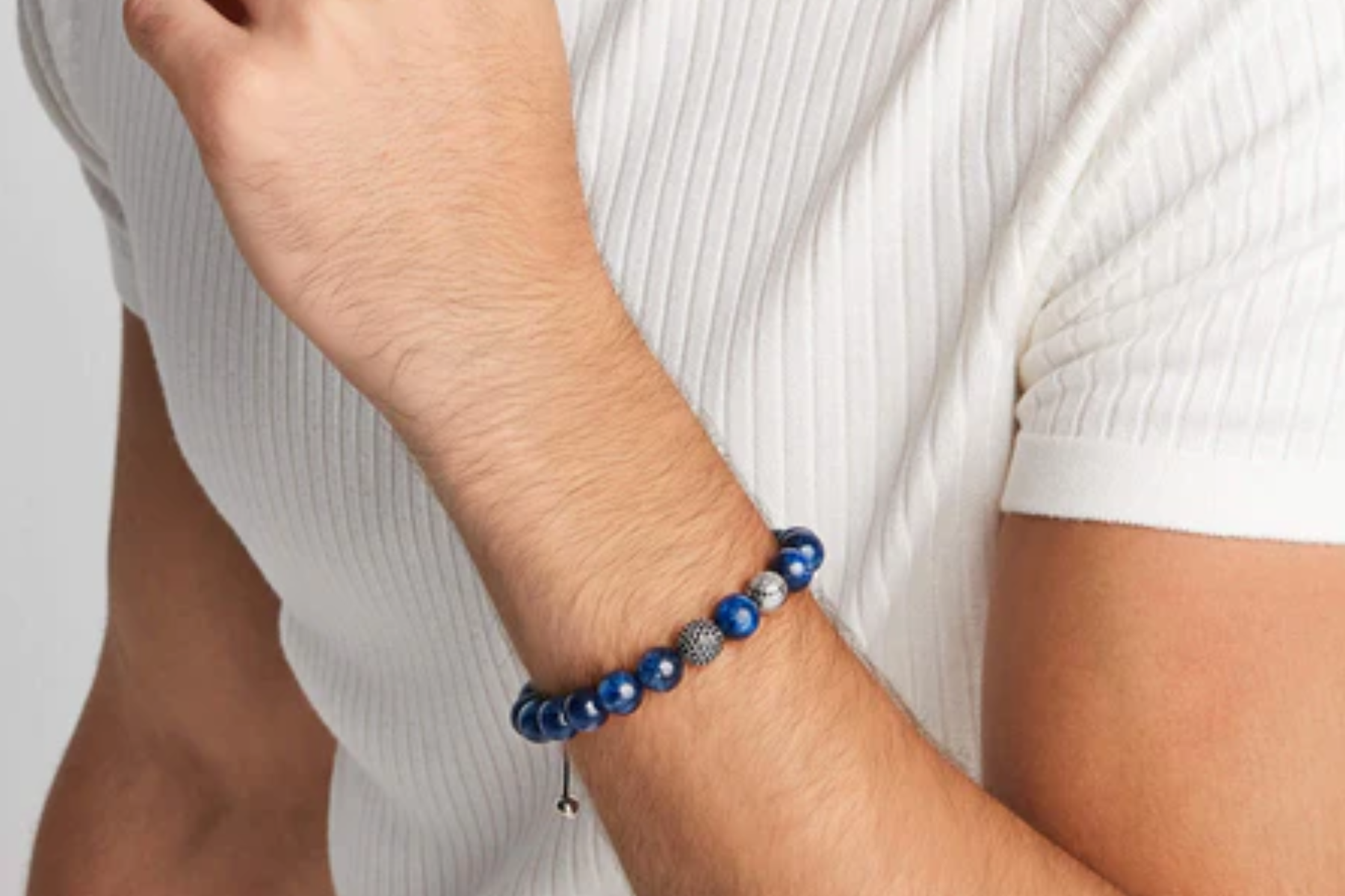 A man in a white shirt wearing blue beaded jewelry with two gray beads as accents