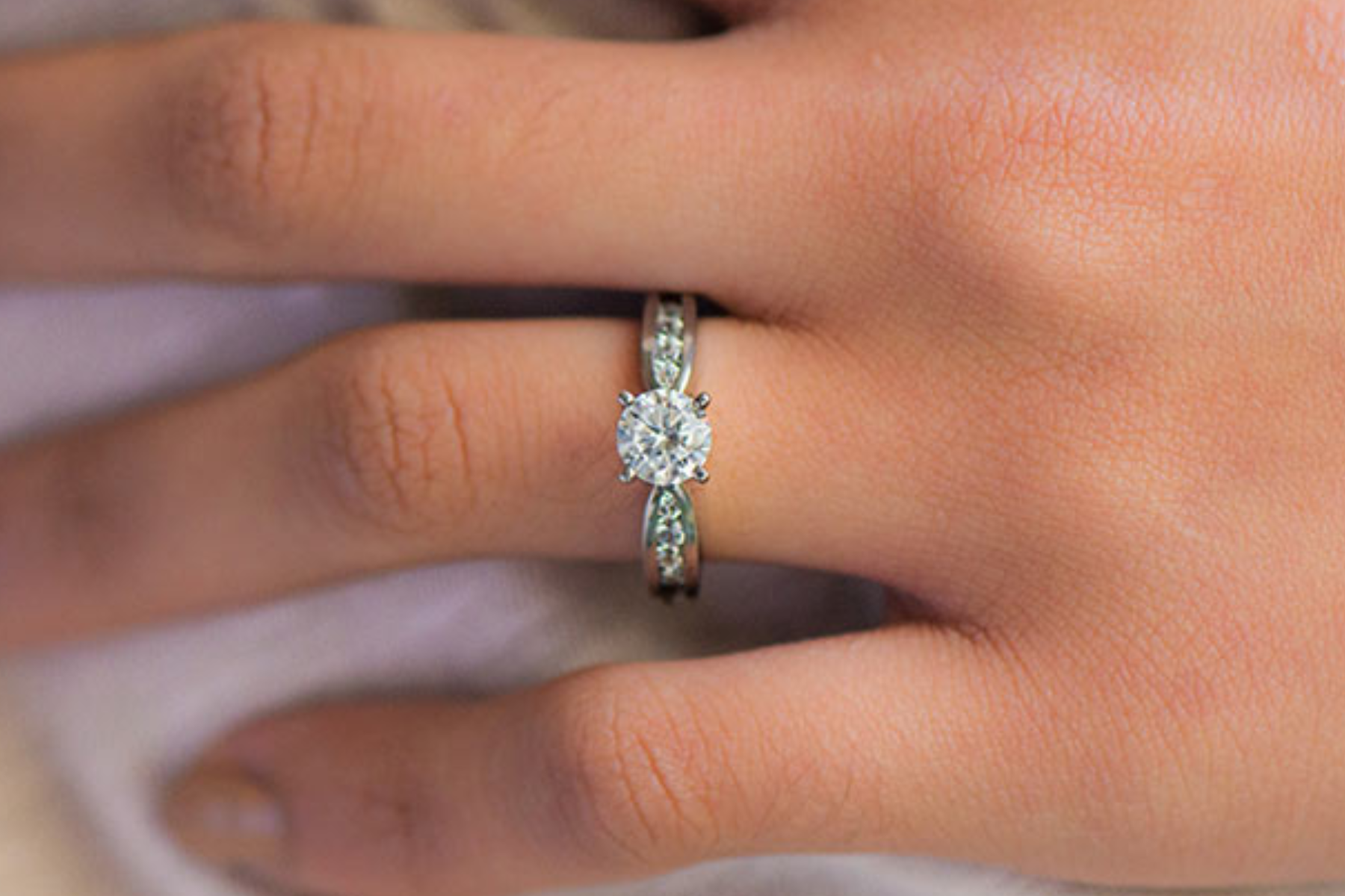 The ring finger of a woman wearing a platinum engagement ring