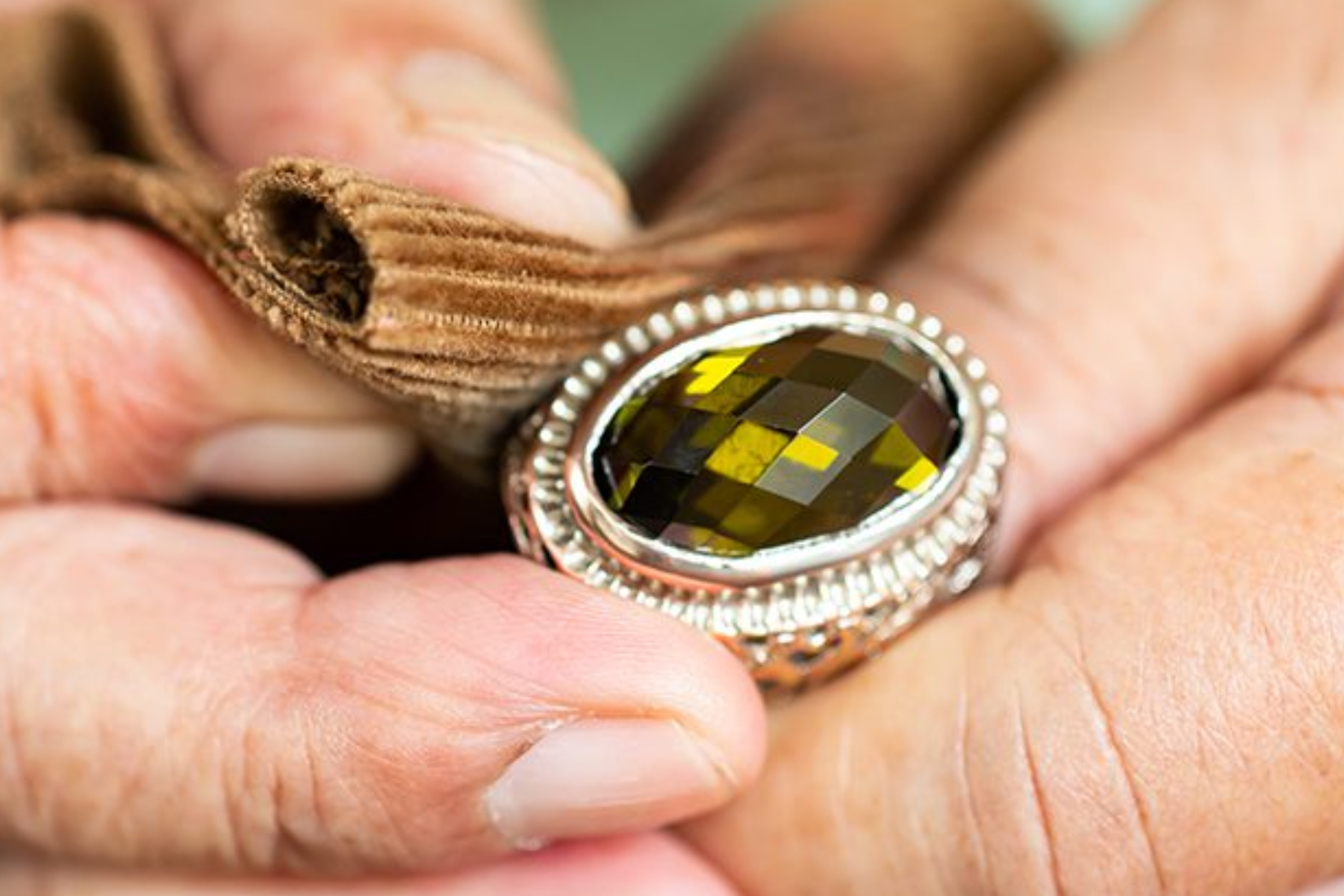 A person's hand polishing a yellow-stoned Victorian-era ring