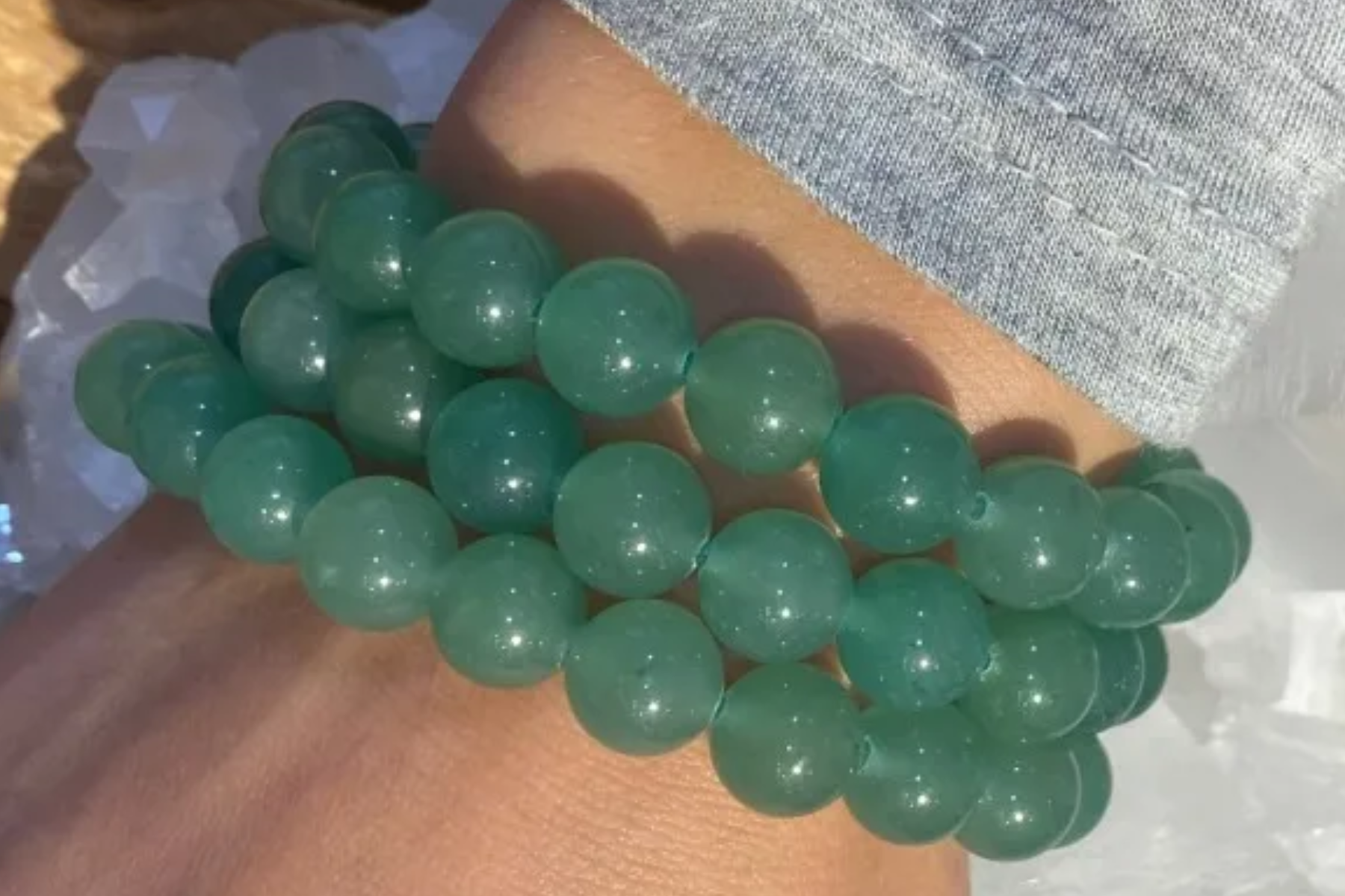 A person's wrist adorned with three bracelets made of aventurine
