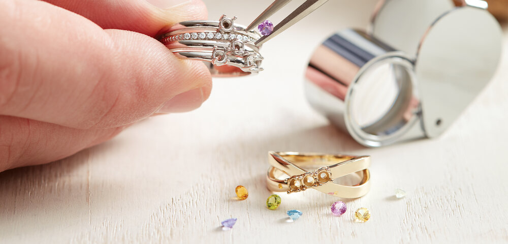 A hand placing colored gemstones into a platinum ring