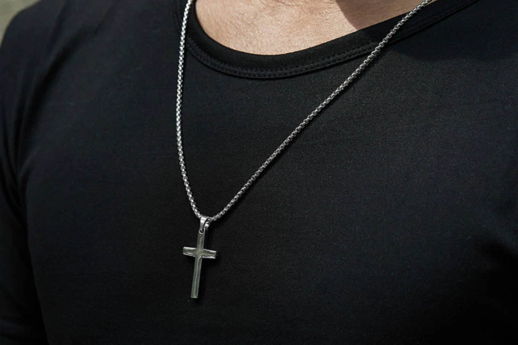 A man in a simple black shirt and a cross pendant necklace