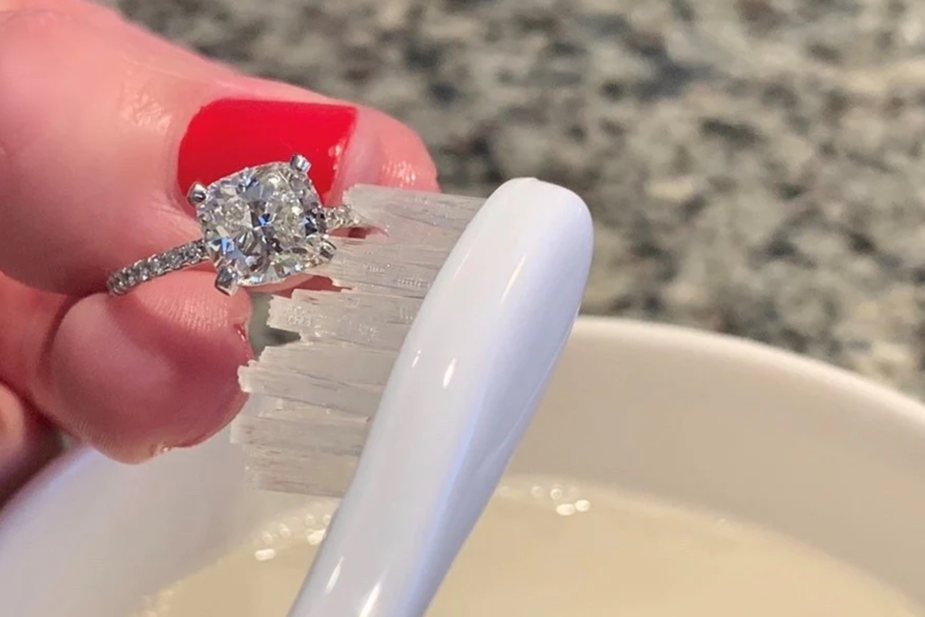 A woman's hand using a soft brush to clean the princess cut ring