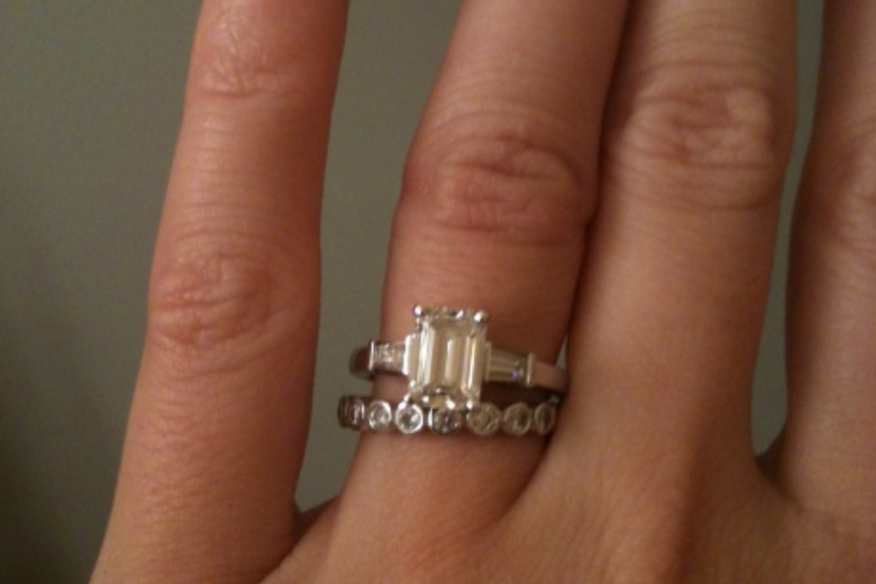 A woman's ring finger is adorned with an emerald-cut and tapered baguettes