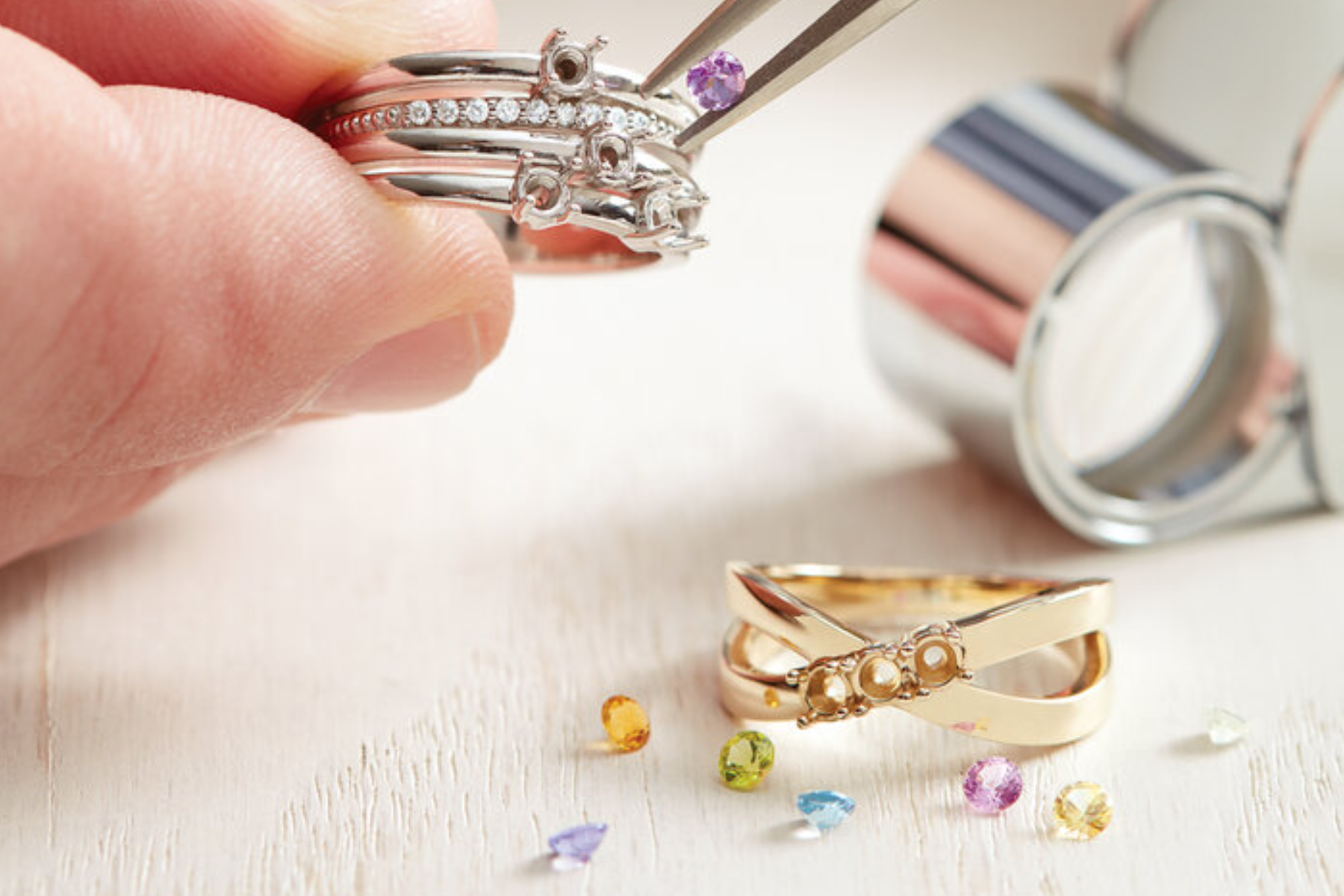 A person's hand placing colorful stones on a customized ring