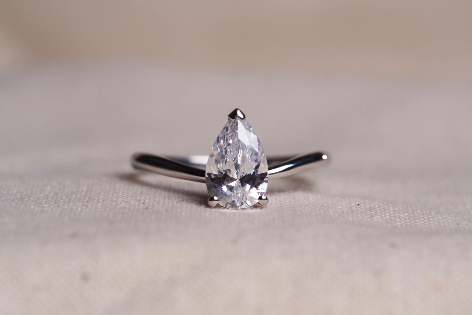 A diamond engagement ring with a pear-shaped cut resting on a floor