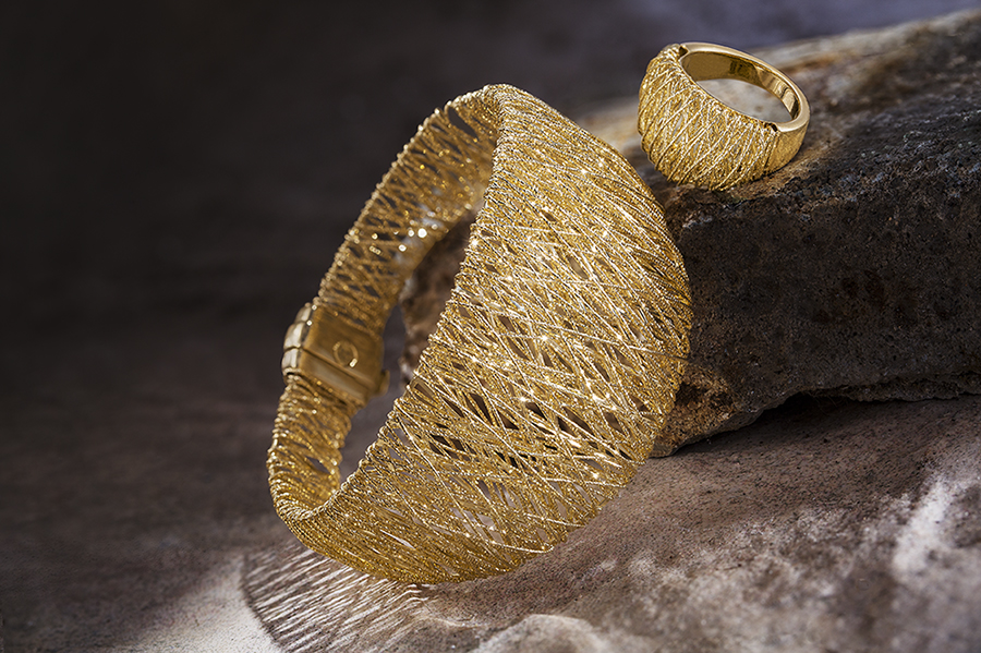 A gold bracelet and ring arranged on a rock