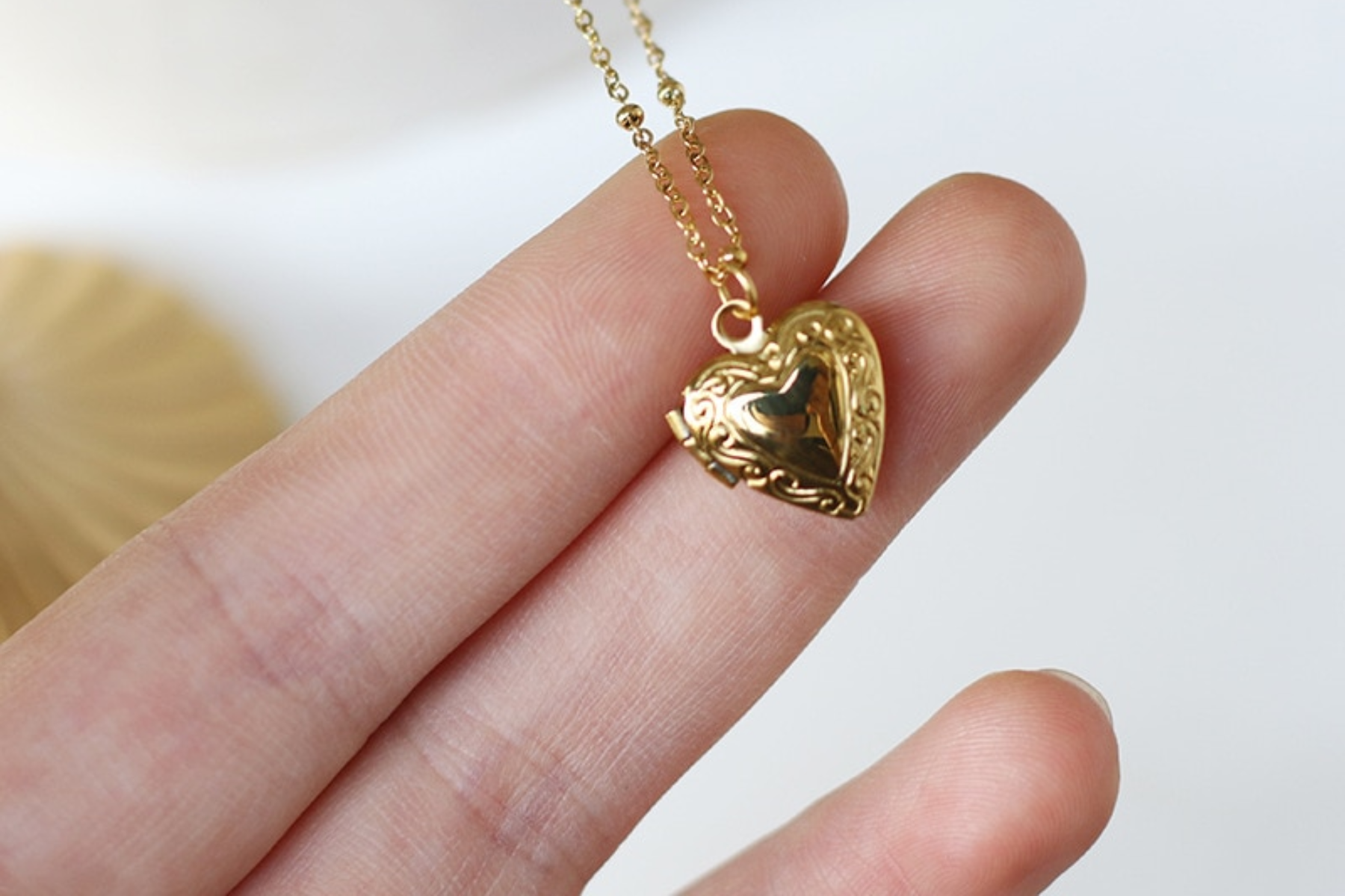 A woman's hand holding a gold heart-shaped pendant necklace