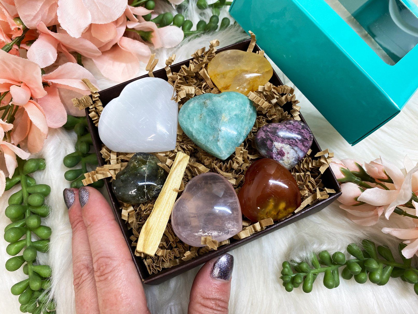 The Amazonite stone, heart-shaped on a box with other different stones as a gift, with a girl's hand holding it