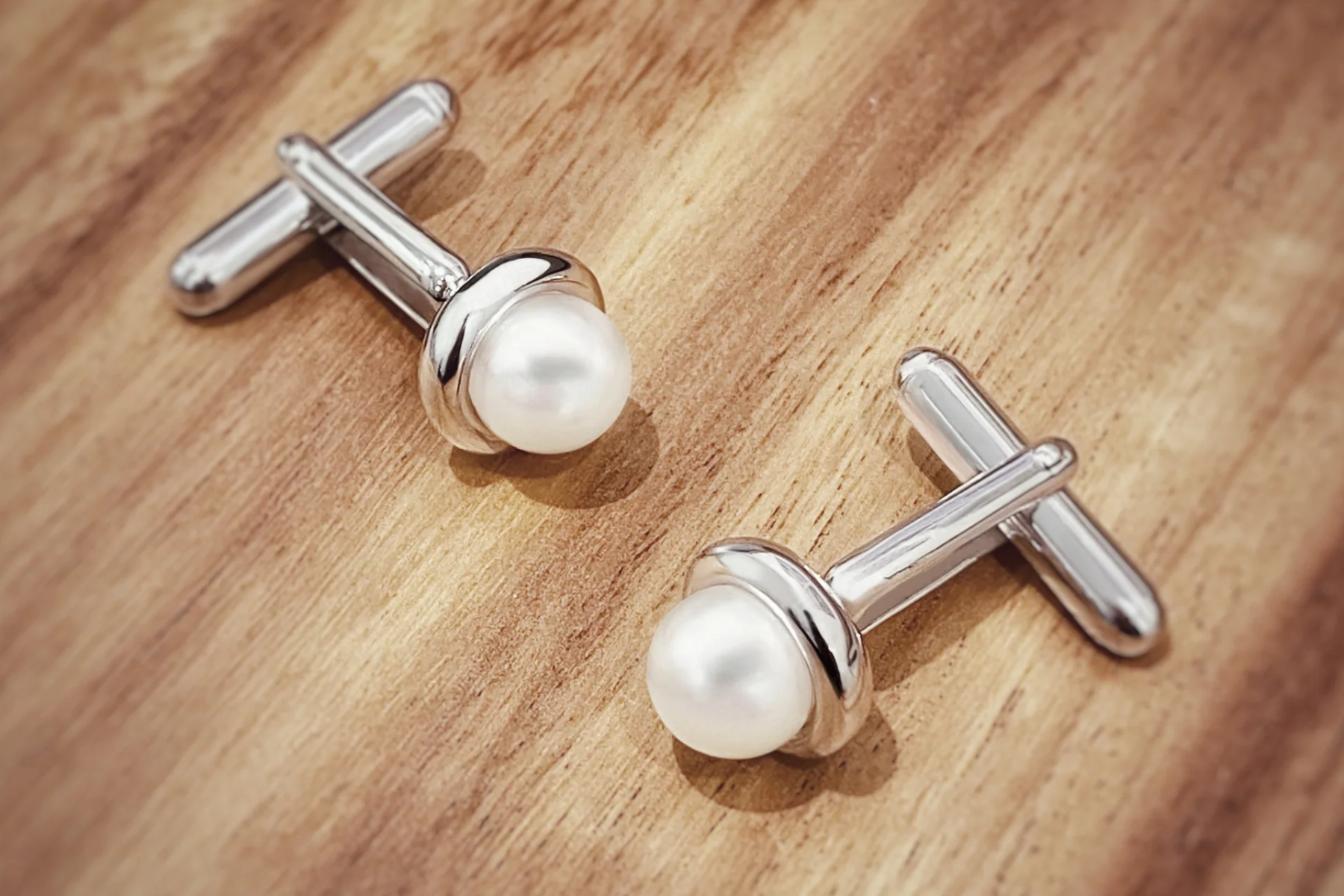 A pair of pearl cufflinks are displayed on a wooden table