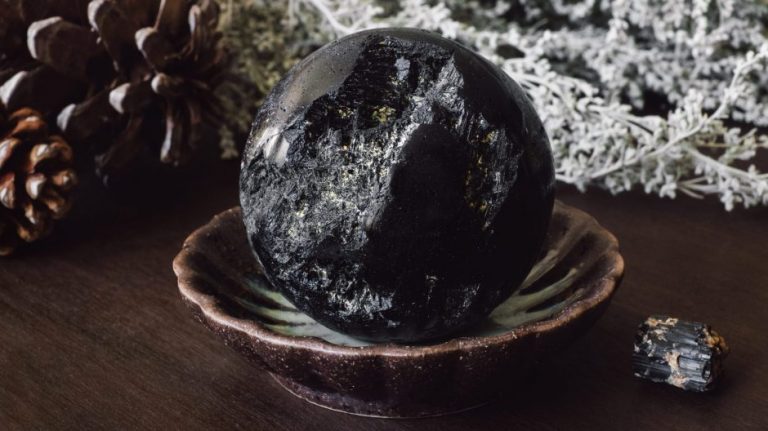 Black tourmaline crystal in a small bowl with pinecone and white flowers beside it