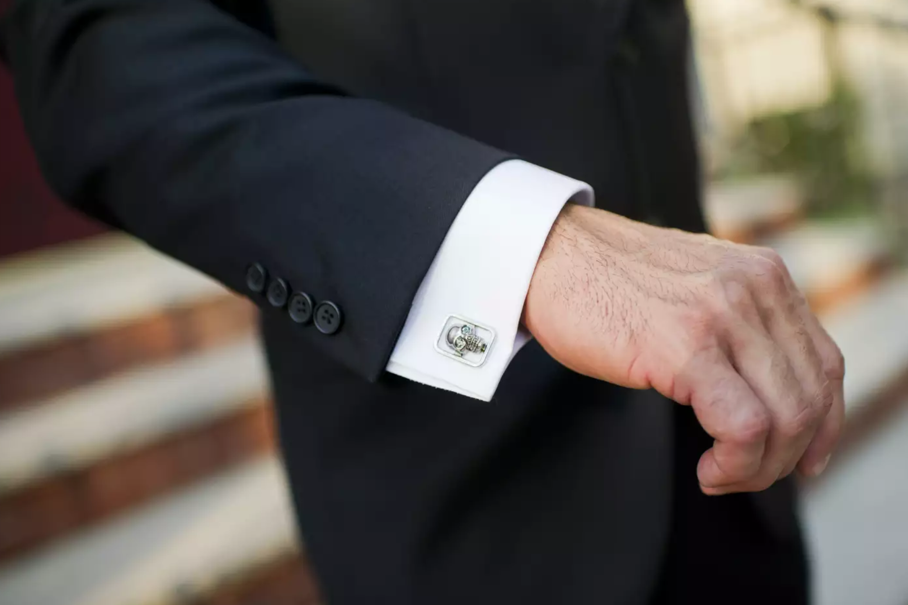 A close-up image of a man's hand wearing a formal suit, with a focus on his skull-shaped cufflink