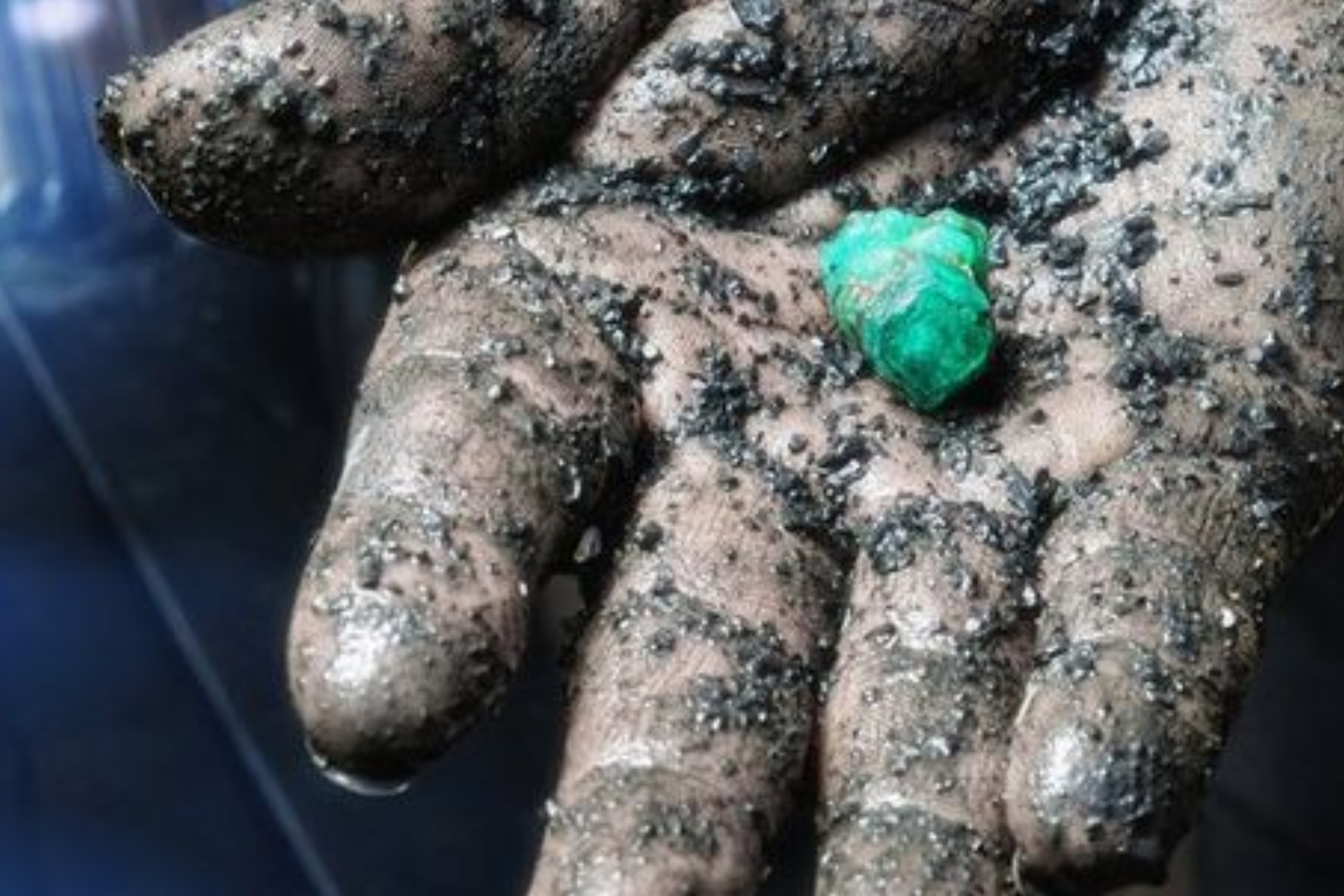 A muddy hand holds a little piece of mined green gemstones