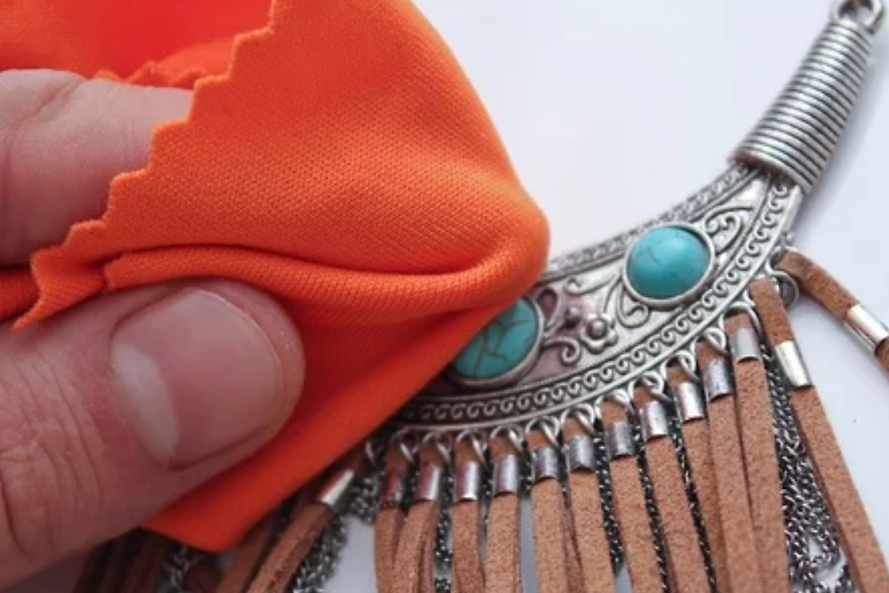 The hand of a man polishing a turquoise necklace with orange cotton