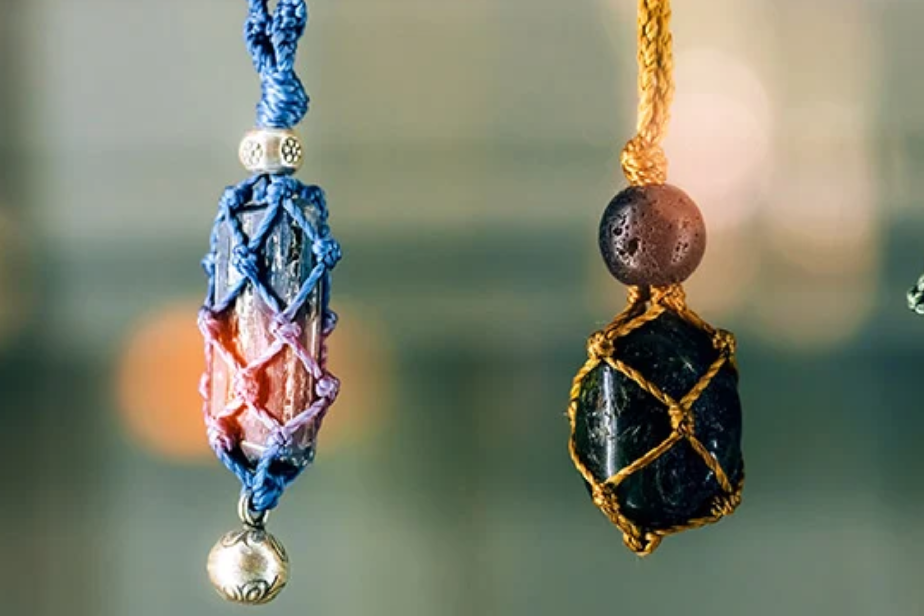 A photograph of two necklaces, one with blue beads and the other with yellow beads, both featuring a chakra pendant. The background is blurred and indistinct
