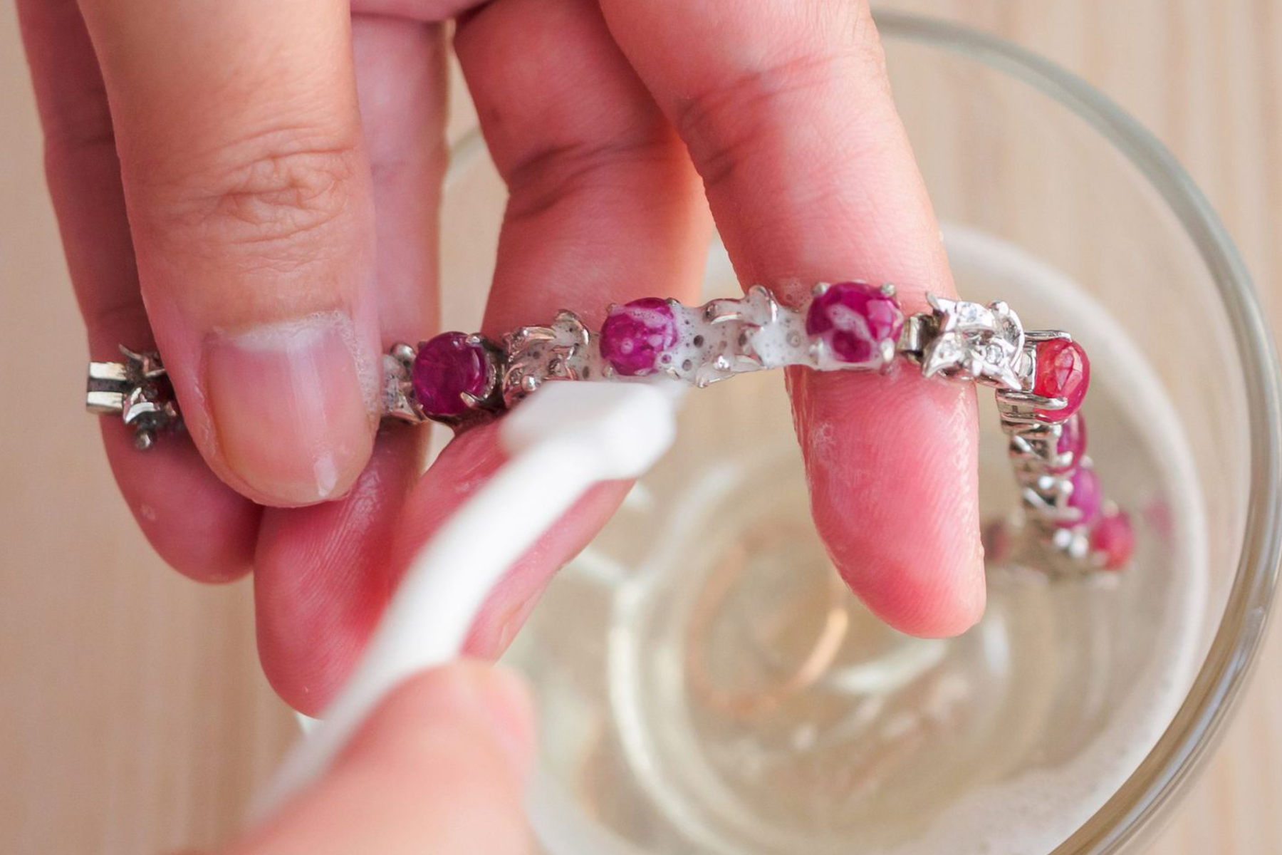 A woman's hand cleaning elegant pink bracelets with a soft brush and water